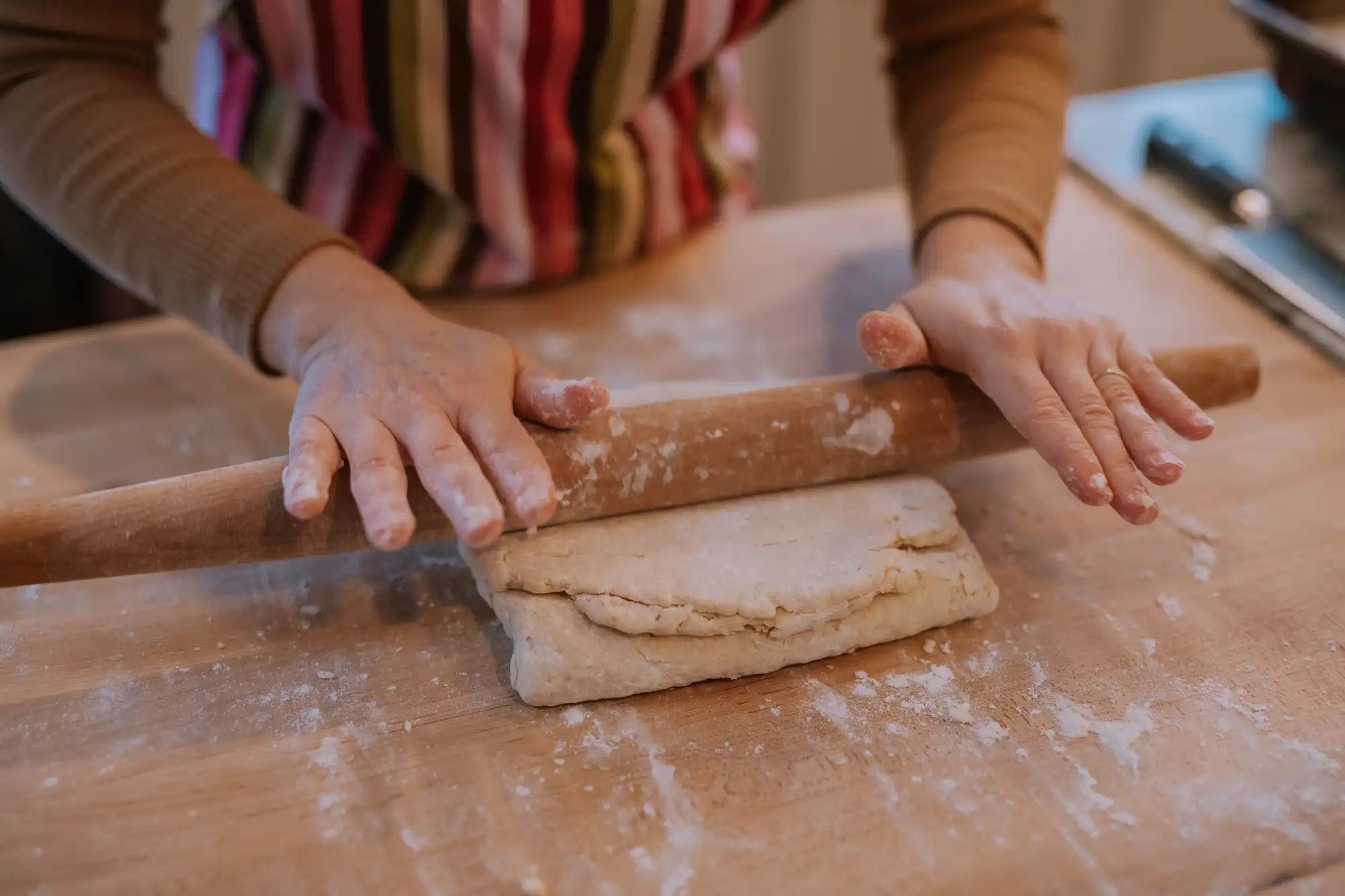 Two hands rolling out folded over biscuit dough with a wooden rolling pin