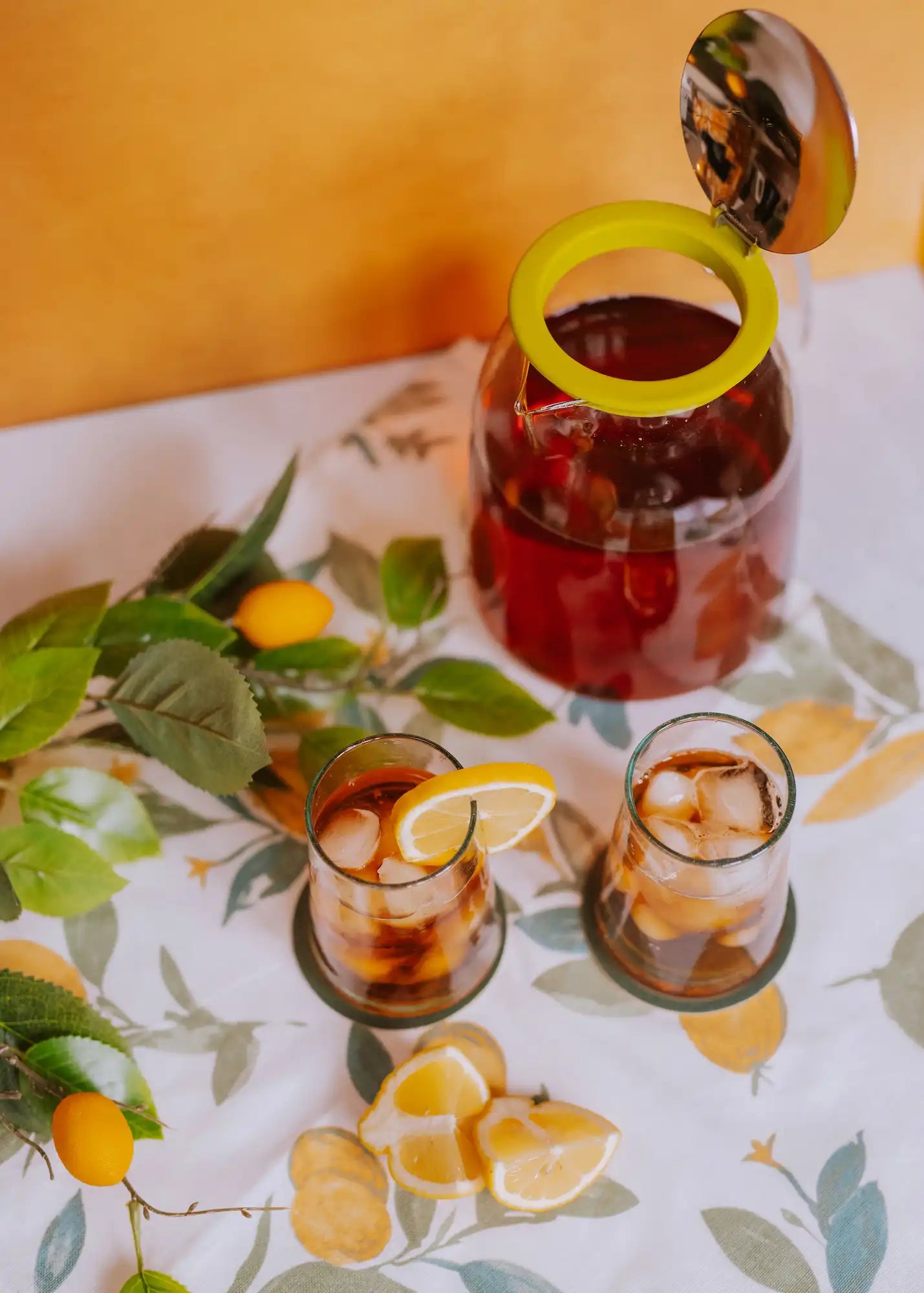 iced tea pitcher with top open and two glasses of black iced tea with lemons