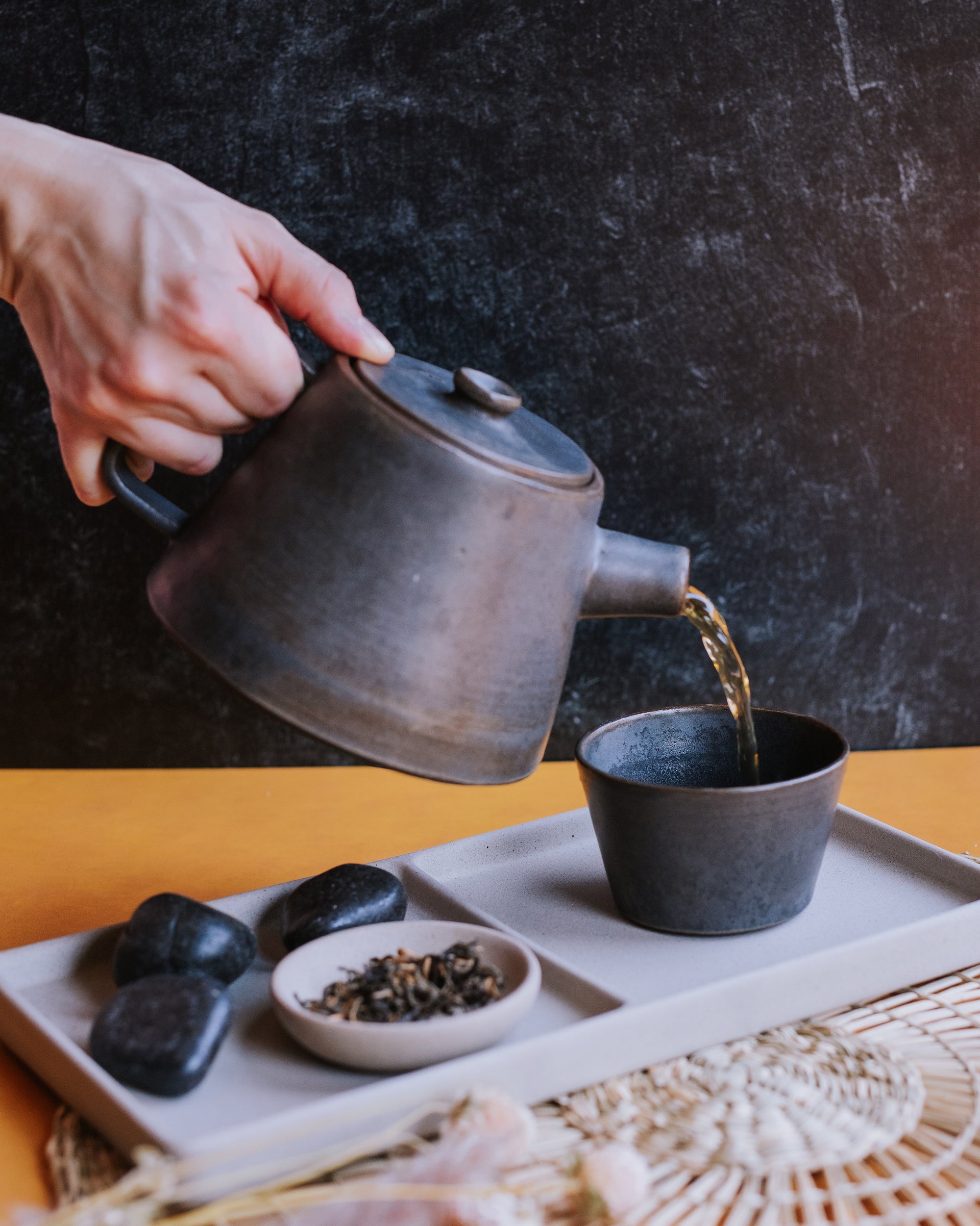 hand pouring black tea from a modern style earthenware teapot with loose leaf black tea in the foreground