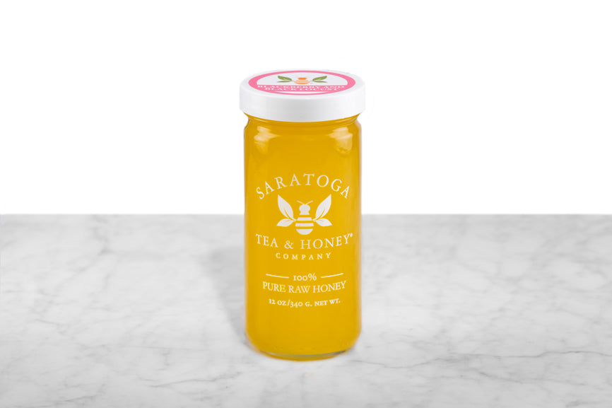 Opaque, golden-hued local Blackberry & Black Locust Honey displayed in a 12oz cylindrical glass jar with a white lid. The logo and the words: "100% Pure Raw Honey" are printed on the jar.