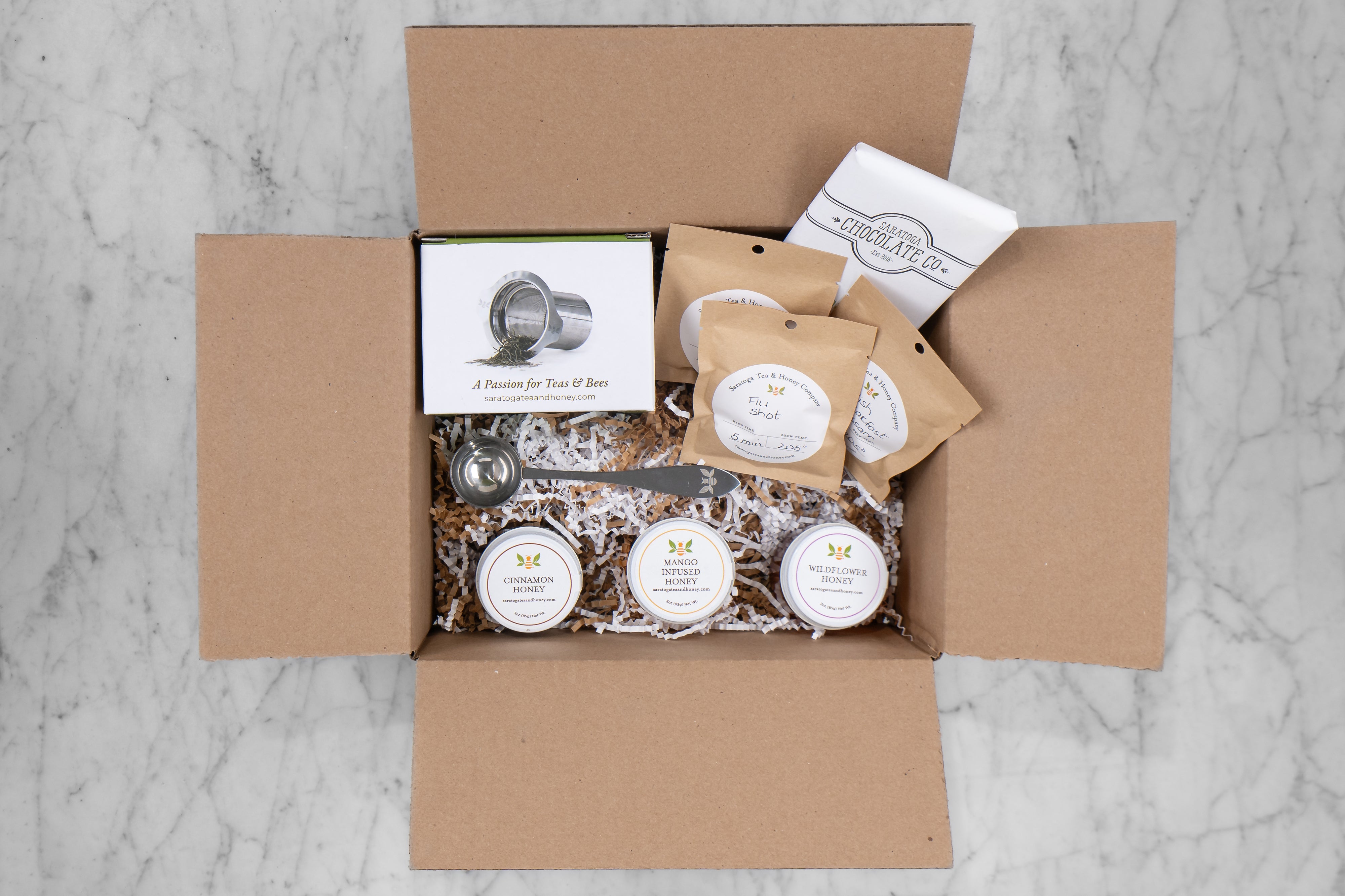 Honey Bee gift set in cardboard box with decorative fill. features three sample teas, three small honeys, tea infuser, tea scoop, and local chocolate bar