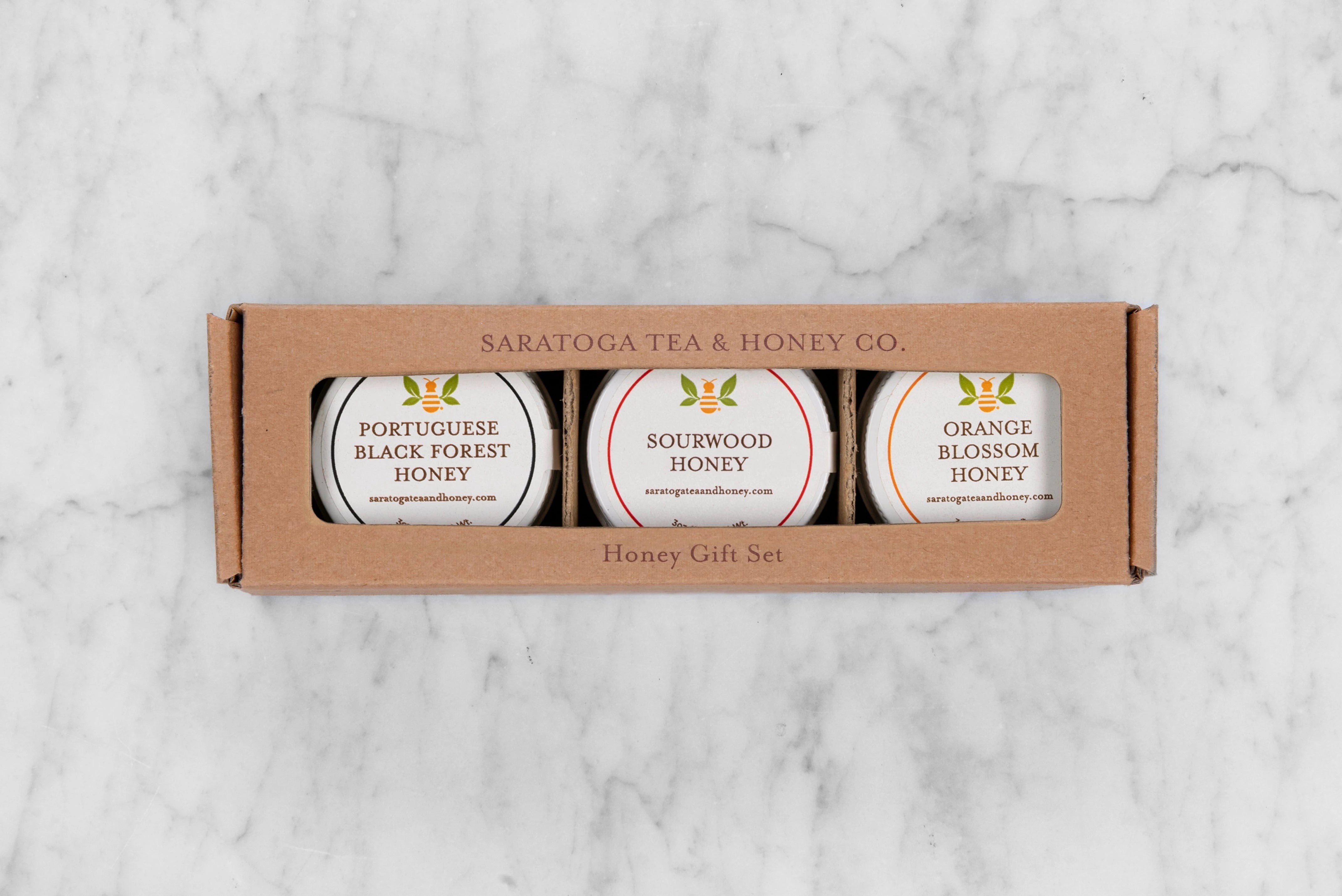 Charcuterie Mini Honey Gift Set with three mini honeys in a brown kraft box with window. From left to right: Portuguese Black Forest Honey, Sourwood Honey, Orange Blossom Honey.