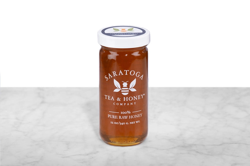 Amber NY wildflower honey in a 12oz clear glass jar branded with the Saratoga Tea & Honey Co. logo and a white top. The logo and the words: "100% Pure Raw Honey" are printed on the jar.