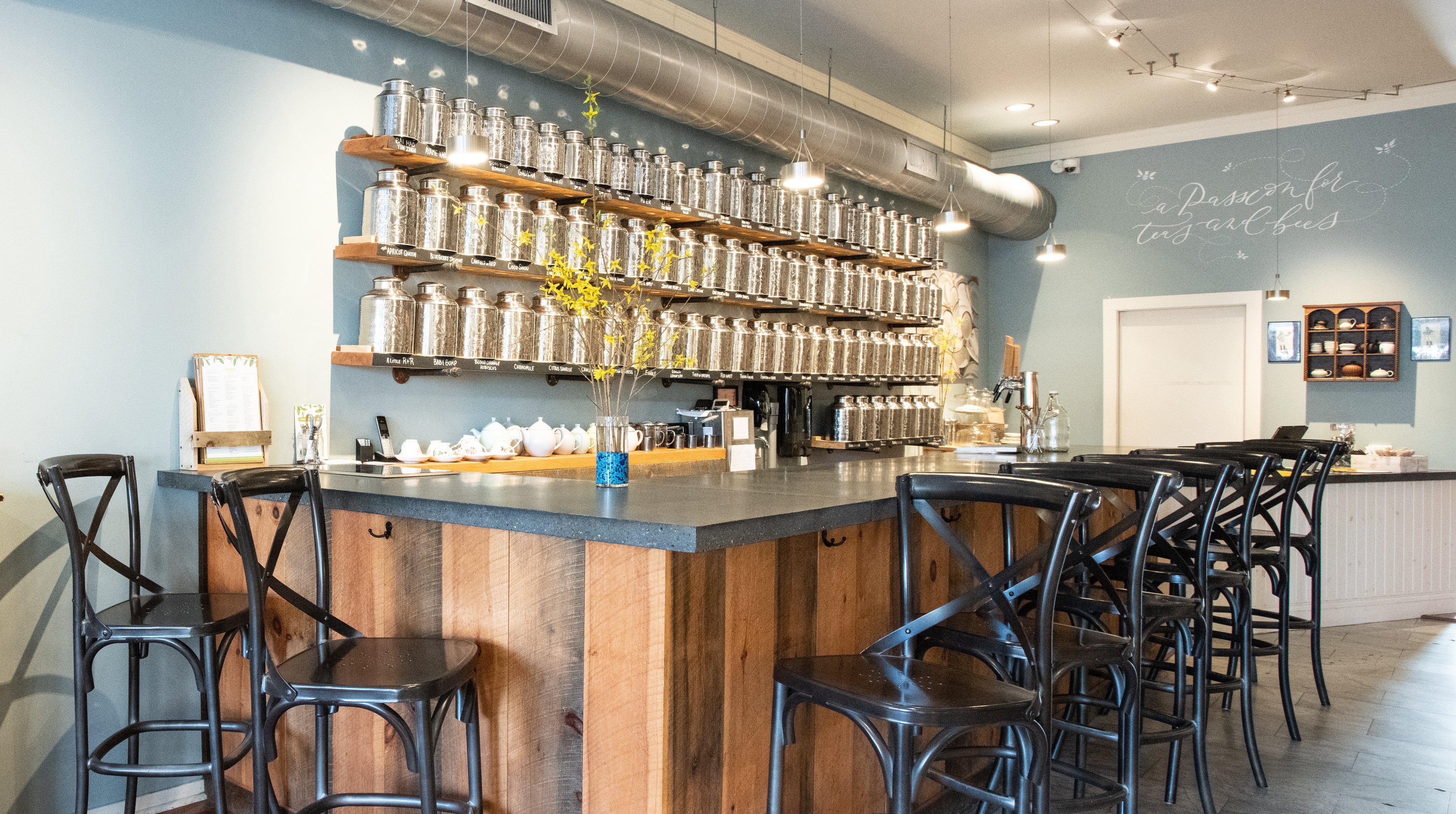 photo of the interior tea bar at Saratoga Tea & Honey Co. featuring 8 bar seats and a wall of silver tea canisters