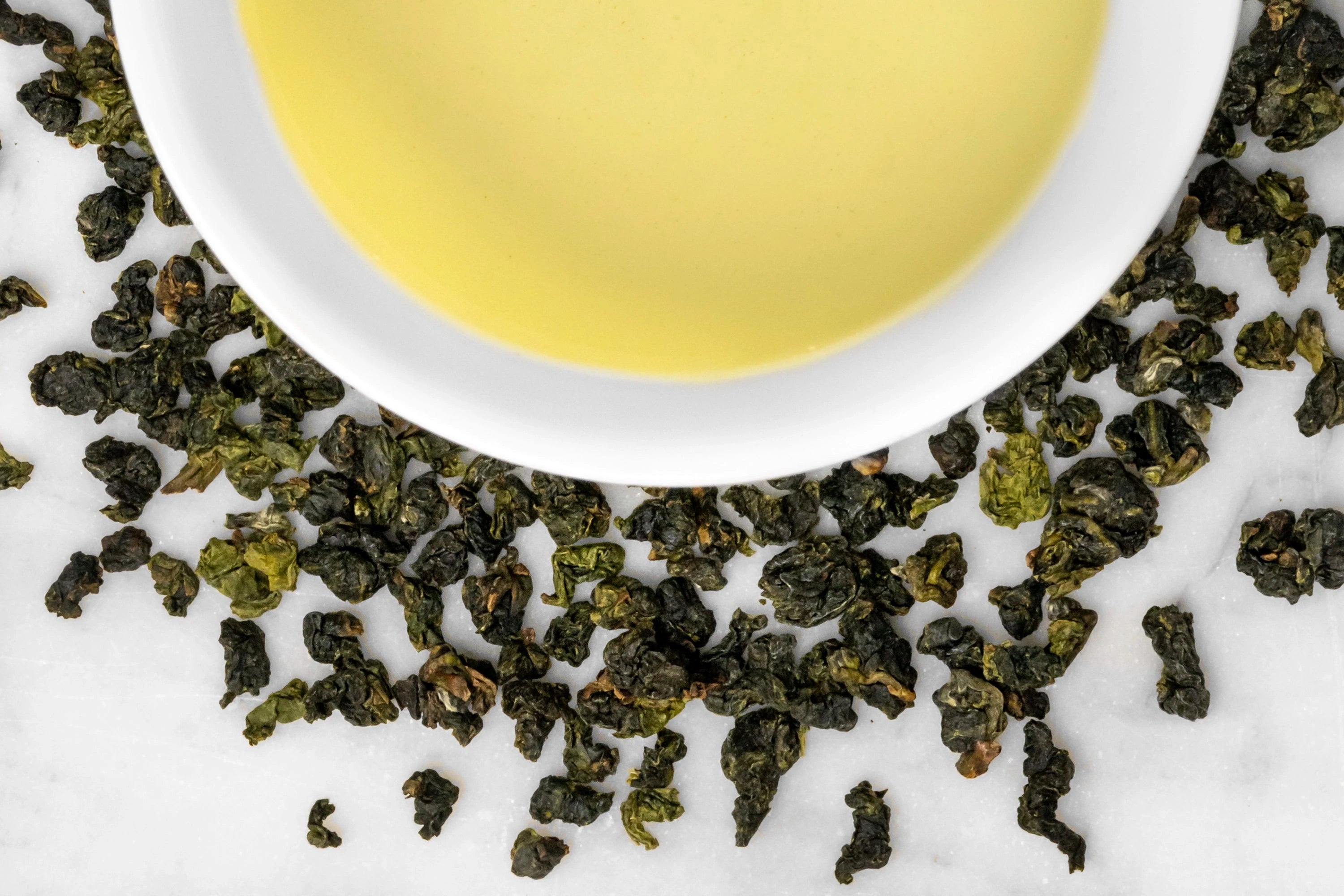 Dong Pian oolong leaves and brewed tea. Lightly oxidized rolled oolong leaves surround a cup of light-yellow brewed Dong Pian.