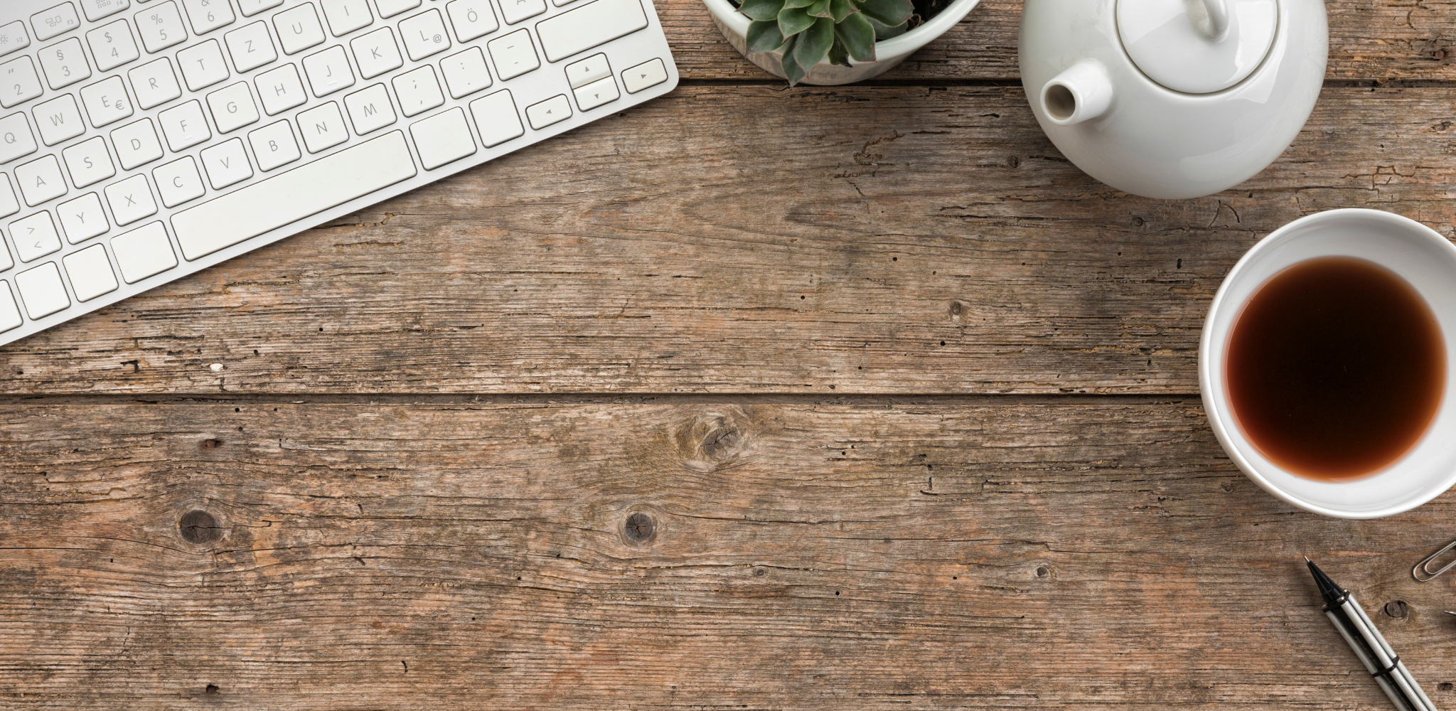 wooden desk with keyboard, teapot, and cup of tea