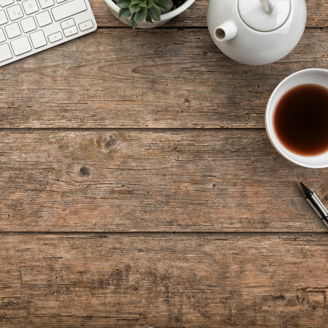 wooden desk with keyboard, teapot, and cup of tea