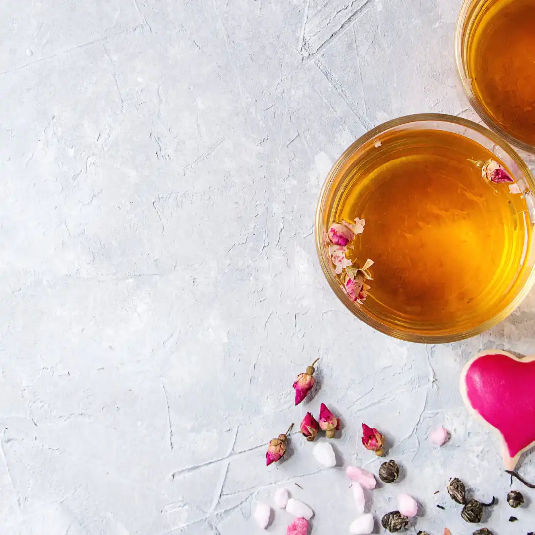 two glass cups of tea with rosebuds and heart cookies