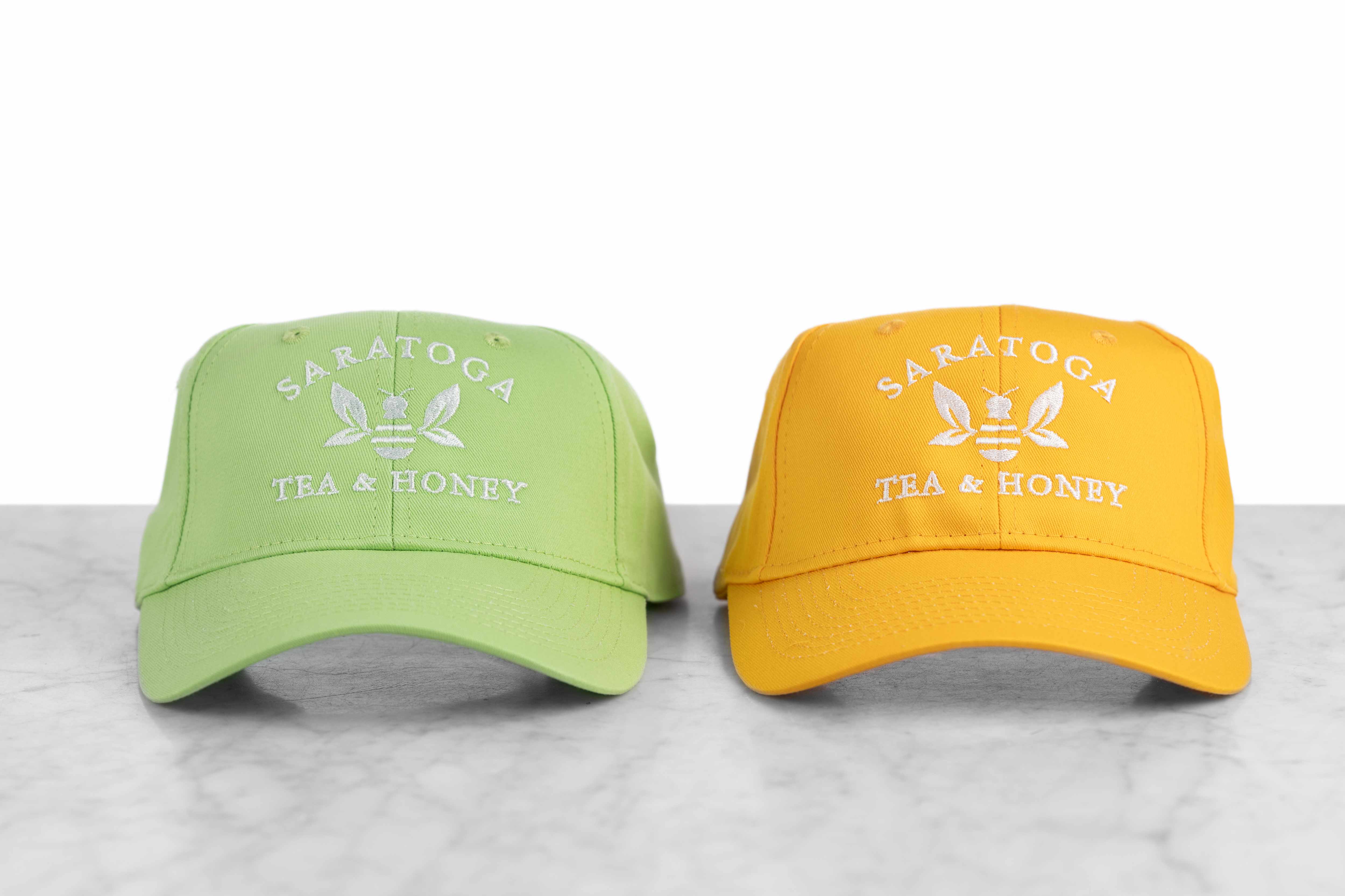 Two baseball caps embroidered with the Saratoga Tea and Honey Company logo.