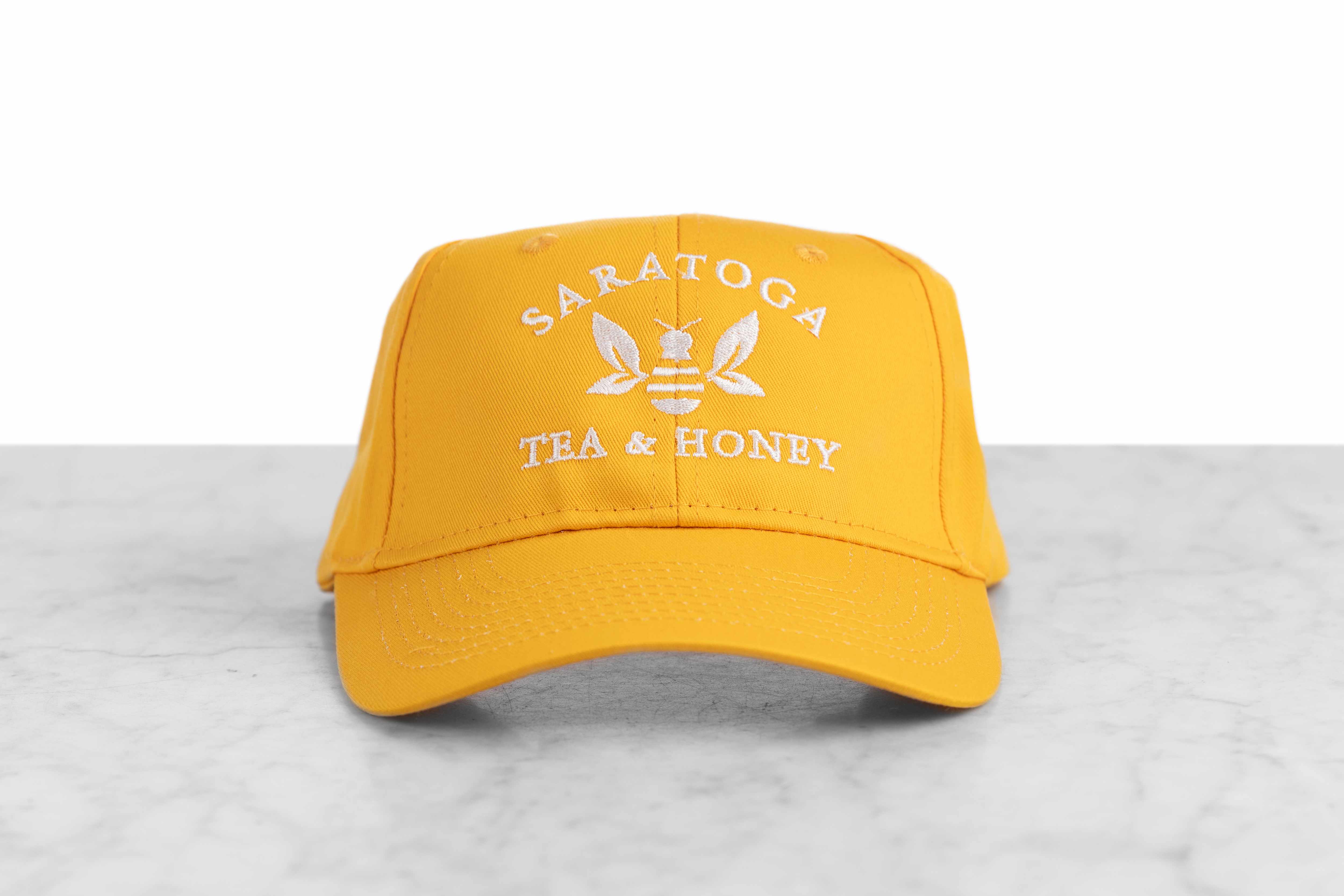 A yellow baseball cap embroidered with the Saratoga Tea and Honey Company logo.