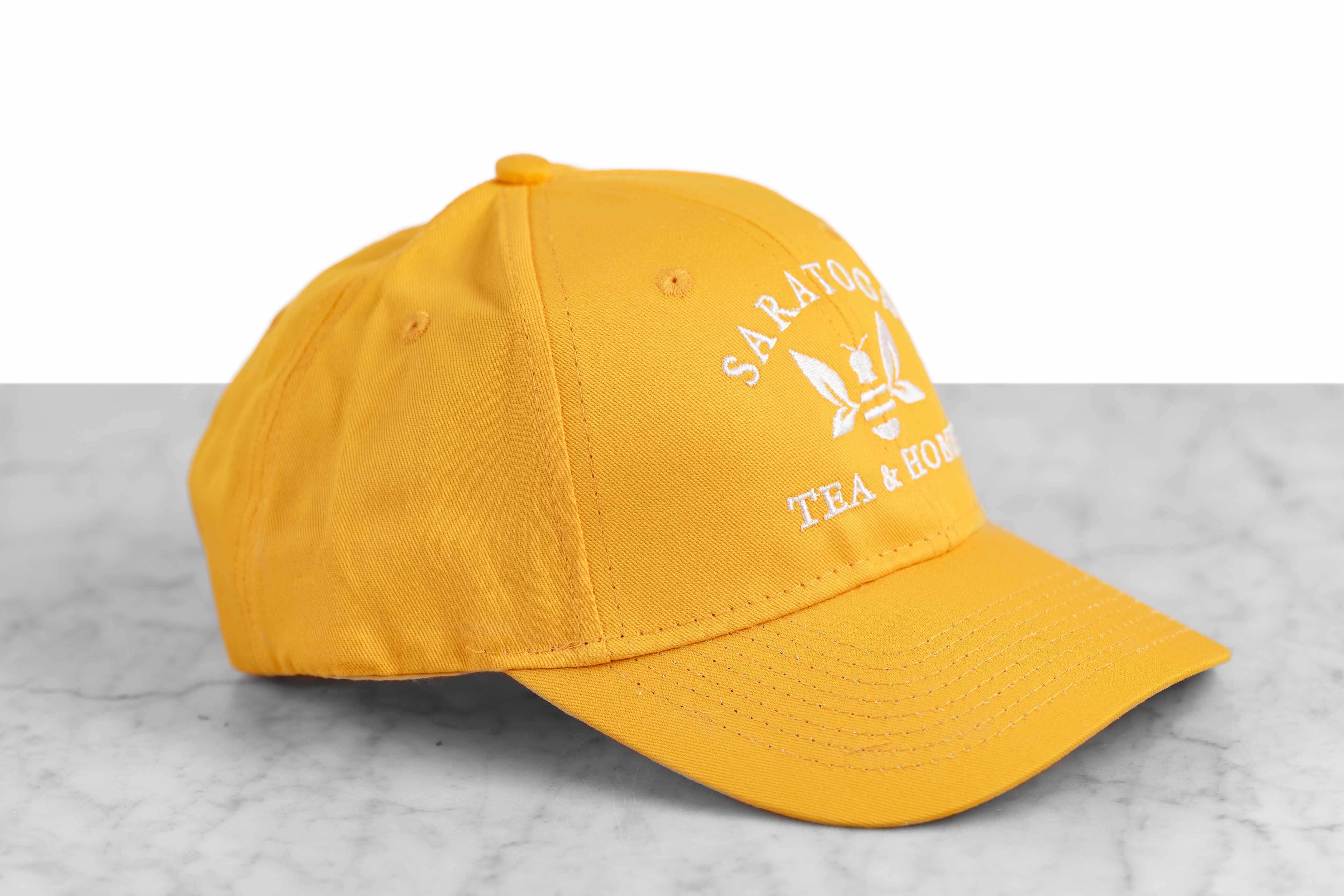 A yellow baseball cap embroidered with the Saratoga Tea and Honey Company logo.