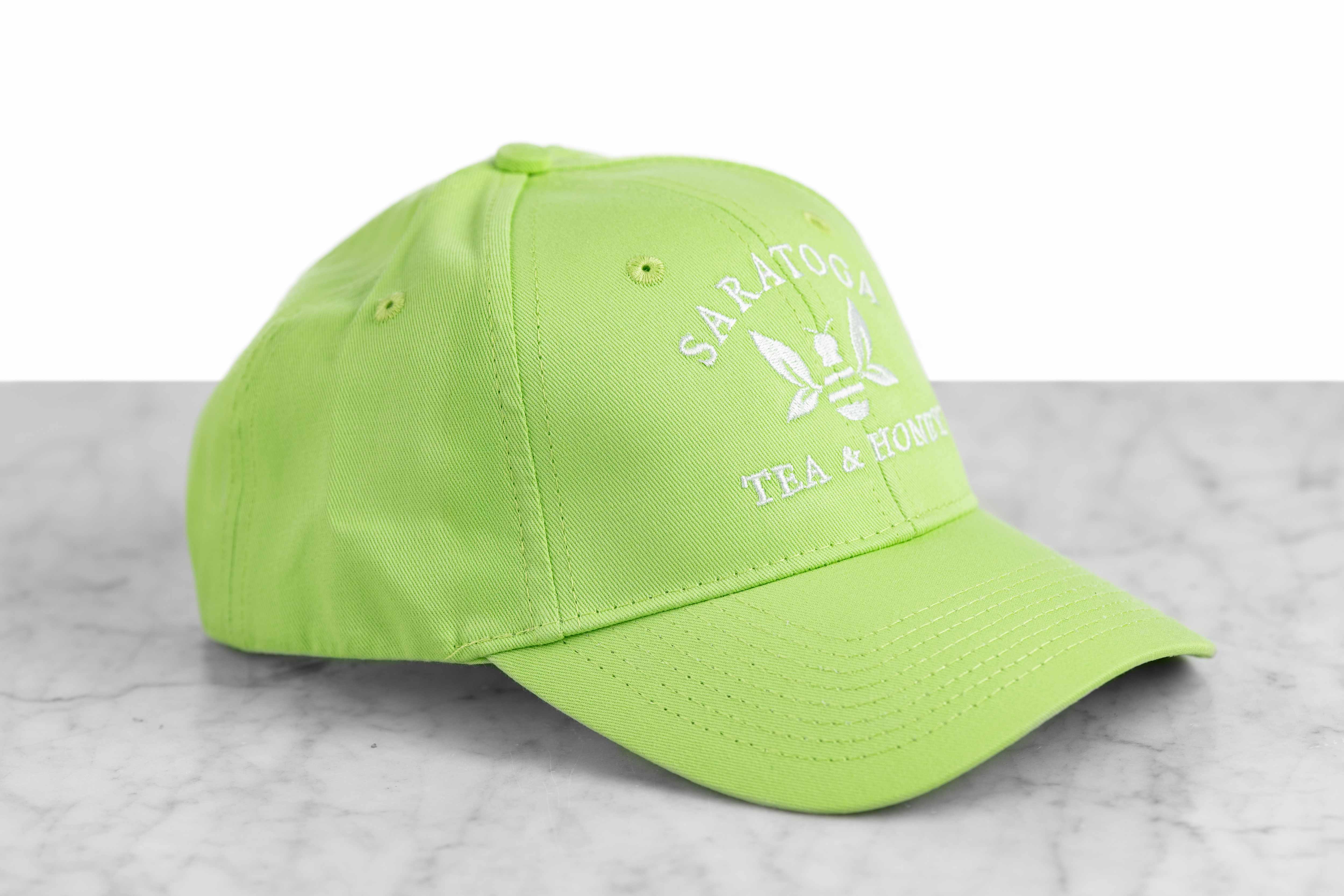 A lime green baseball cap embroidered with the Saratoga Tea and Honey Company logo.