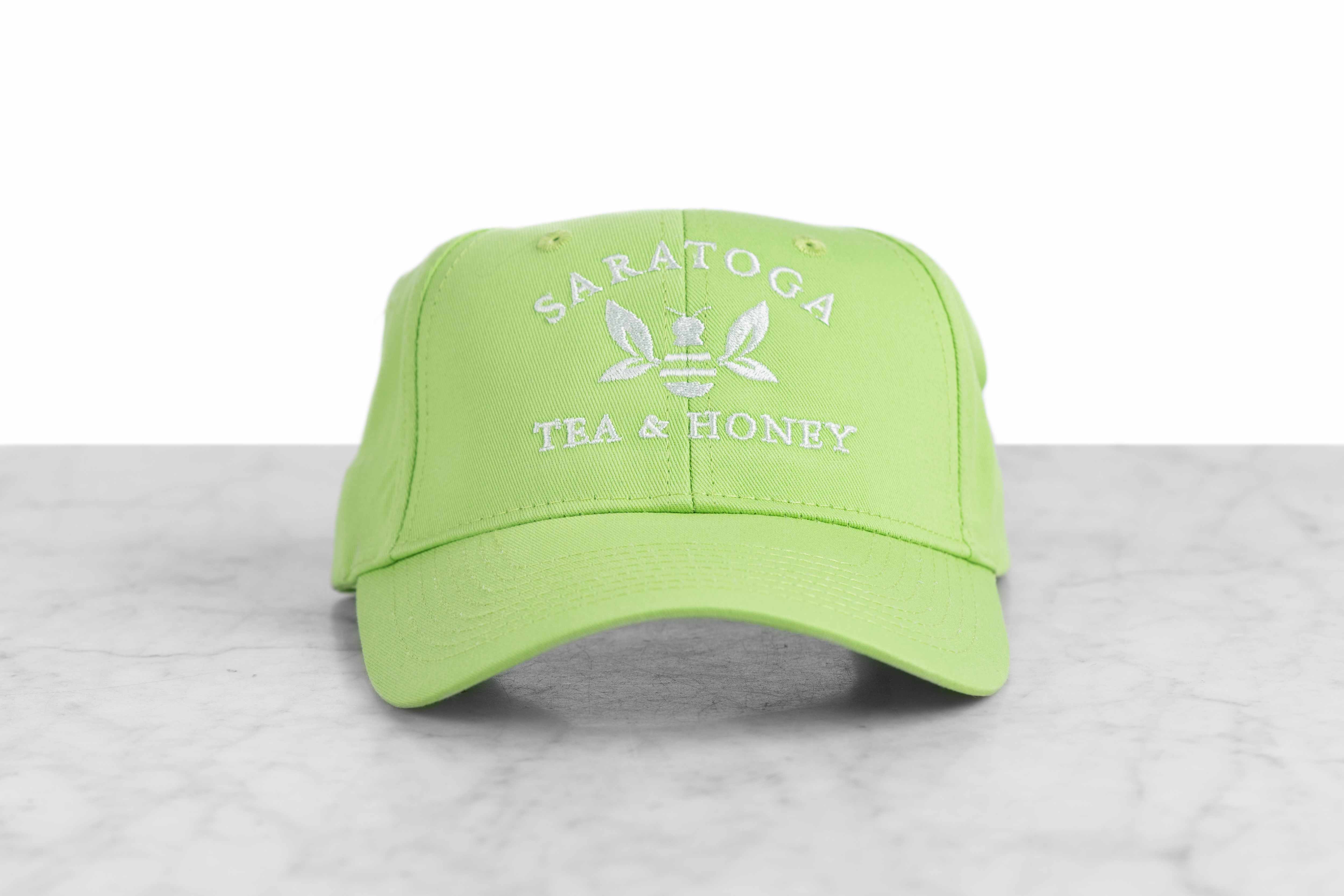 A lime green baseball cap embroidered with the Saratoga Tea and Honey Company logo.