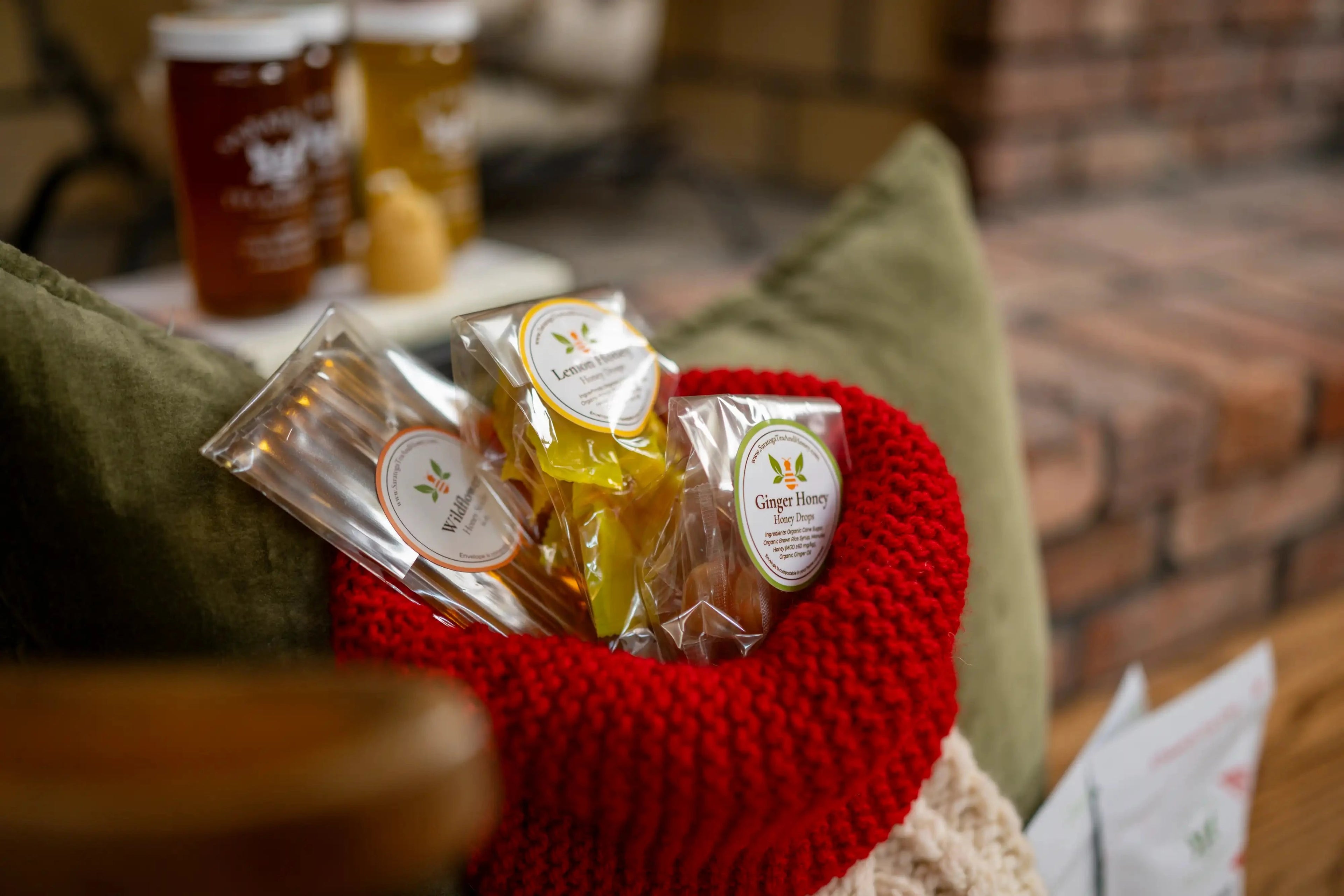 closeup of honey stick gift pack and small packages of honey candy in a ride and white stocking with a fireplace and jars of honey in the background