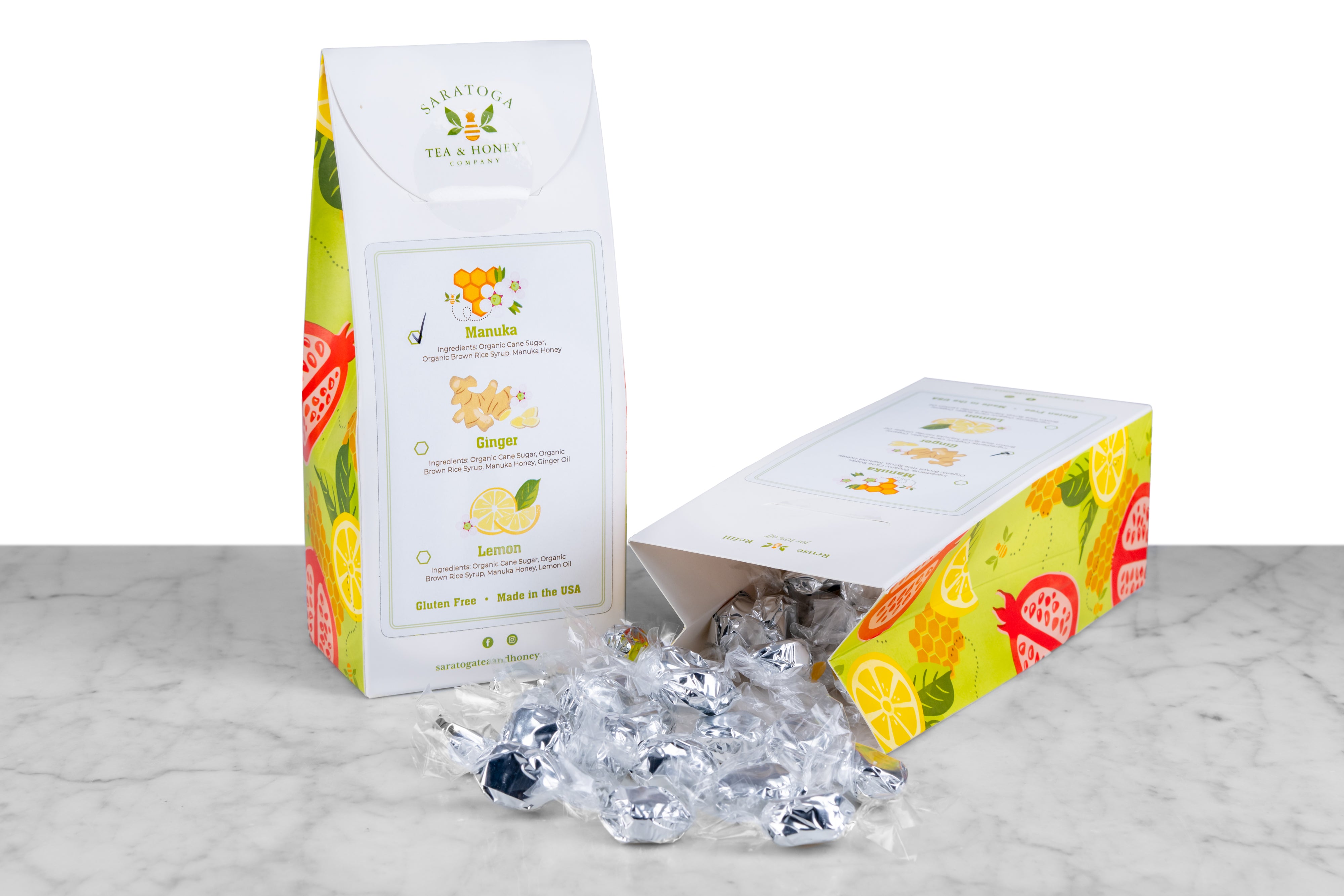 Back view of honey drop box with sticker showing manuka honey, lemon, or ginger flavor variety and spilled open box of foil wrapped honey lozenges 