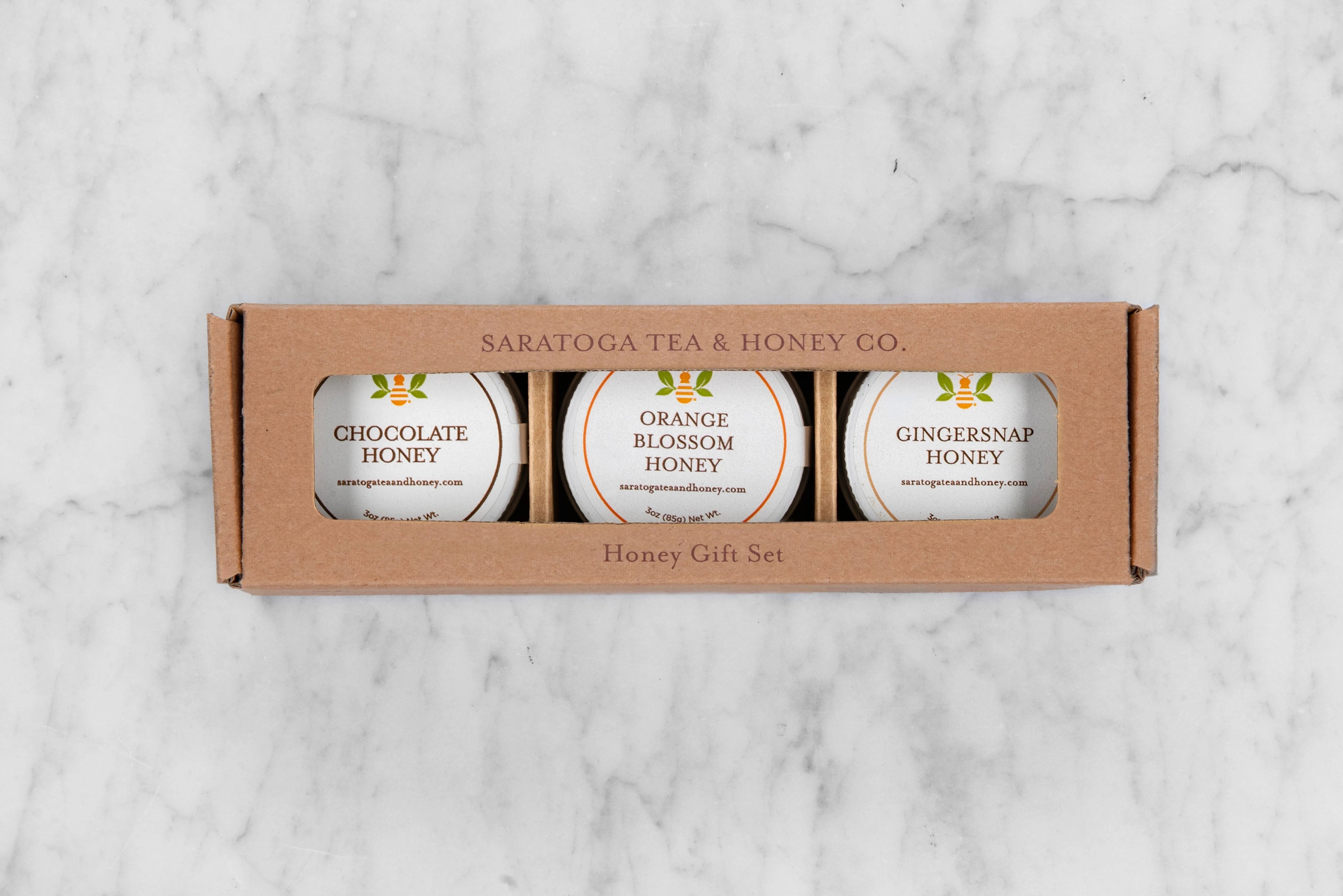 Sweater Weather Honey Trio Gift Set. Three mini 3oz honeys with white labels in a brown kraft box with a window. Features: Chocolate Honey, Orange Blossom Honey, Gingersnap Honey