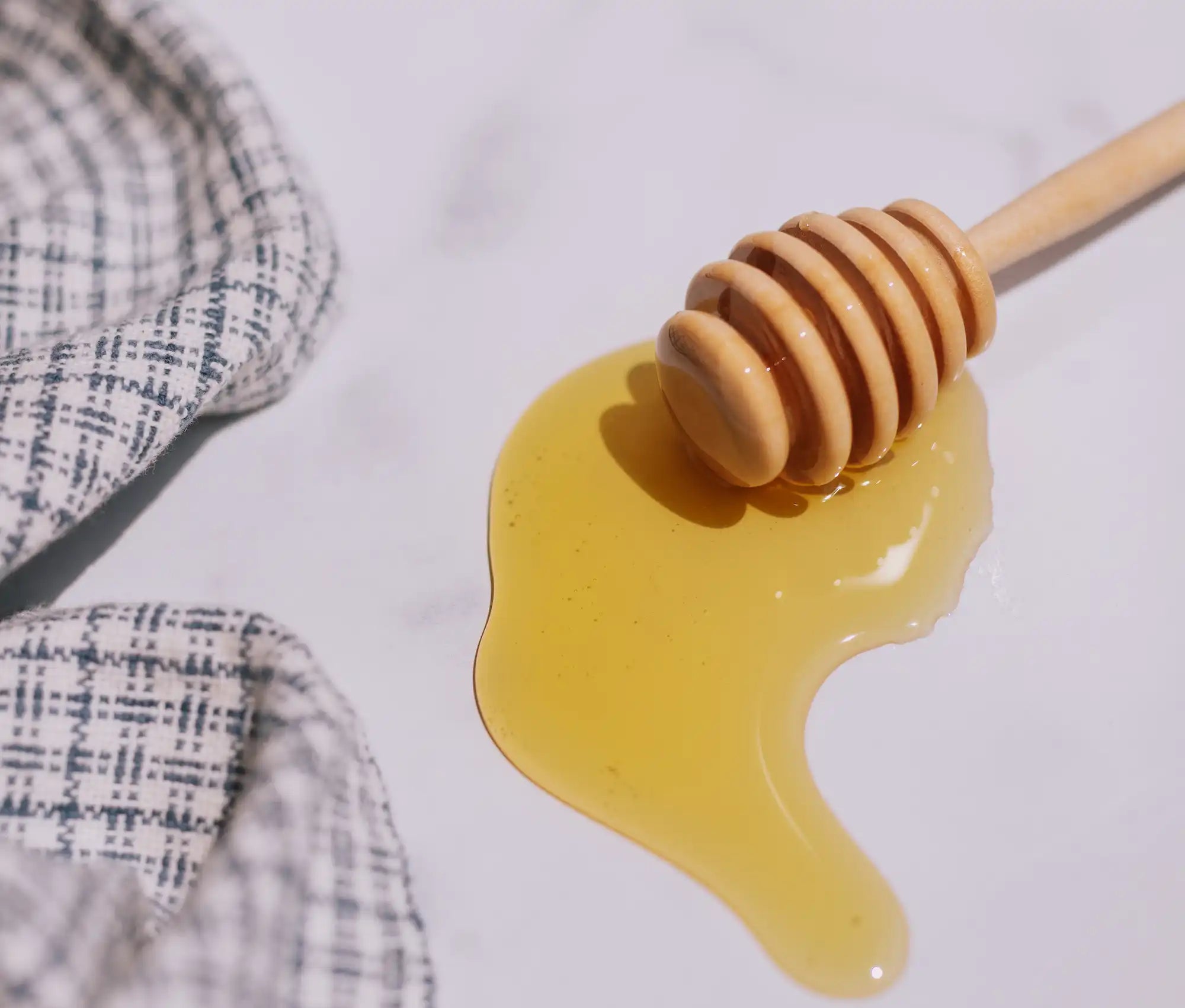 honey drizzled on marble with a wooden honey dipper and blue and white linens