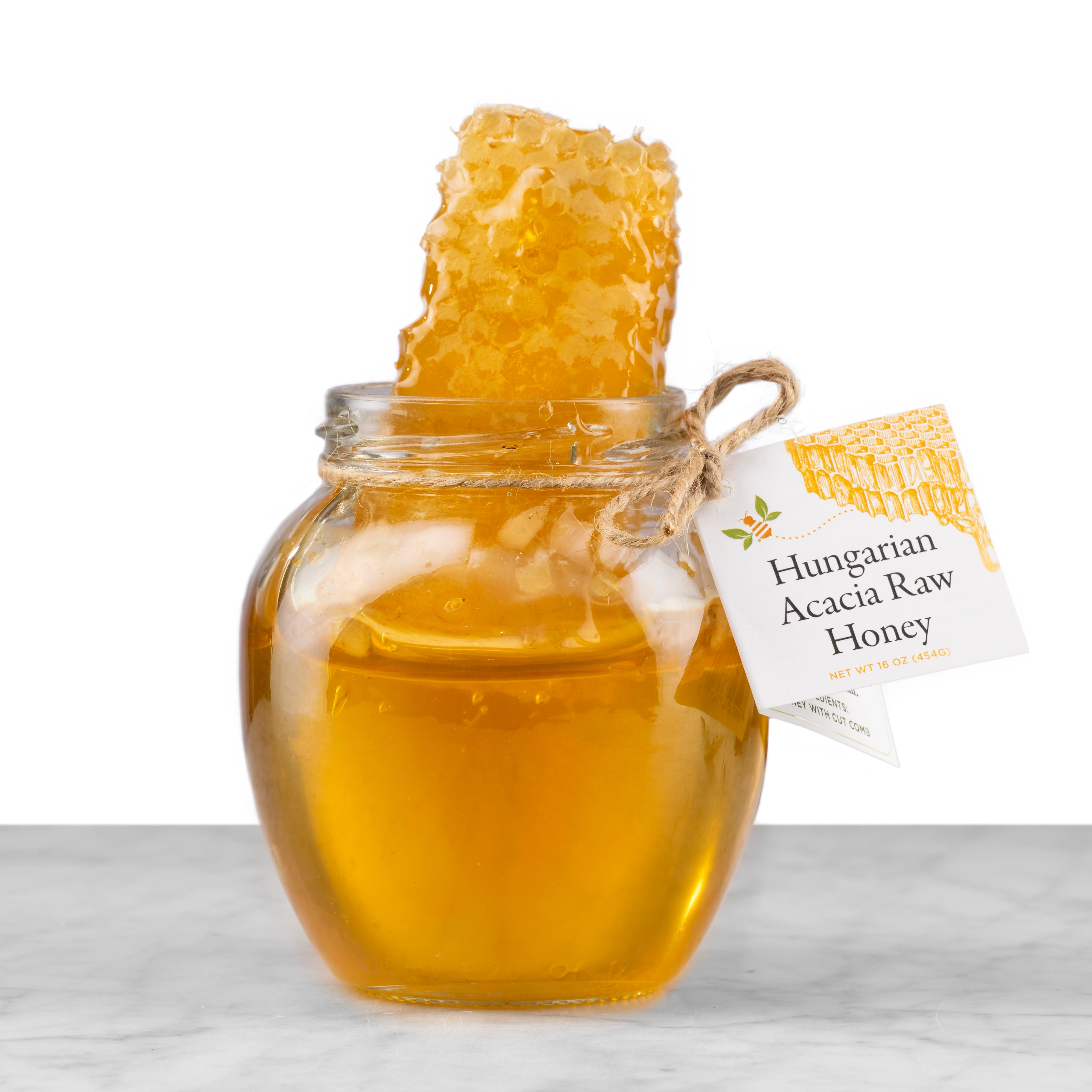 A rounded jar of Hungarian Acacia Raw Honey with a brick of honeycomb.