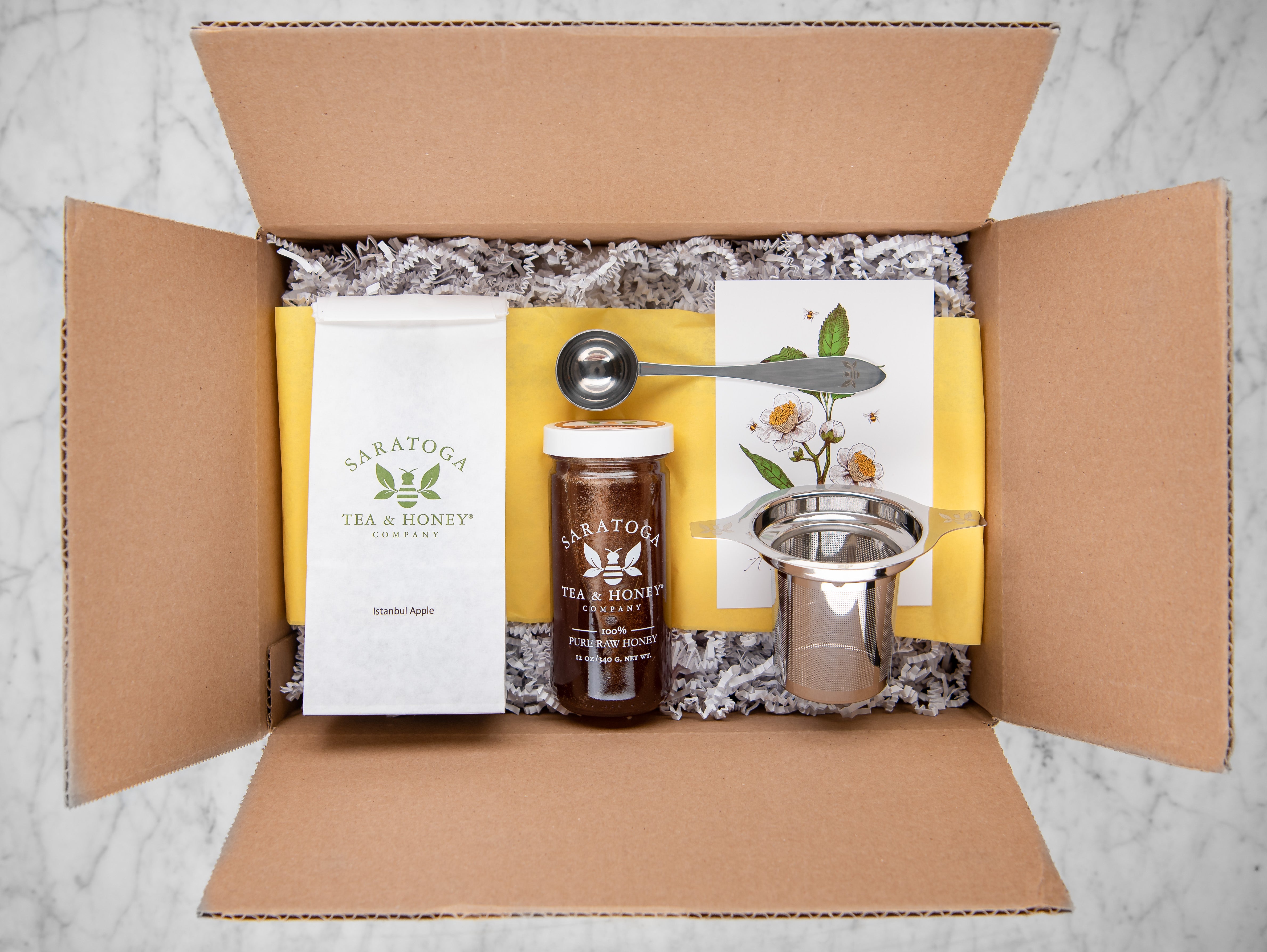 fall seasons tea and honey box: cardboard box with gift fill, instanbul apple, cinnamon honey, a stainless steel infuser, and a tea scoop