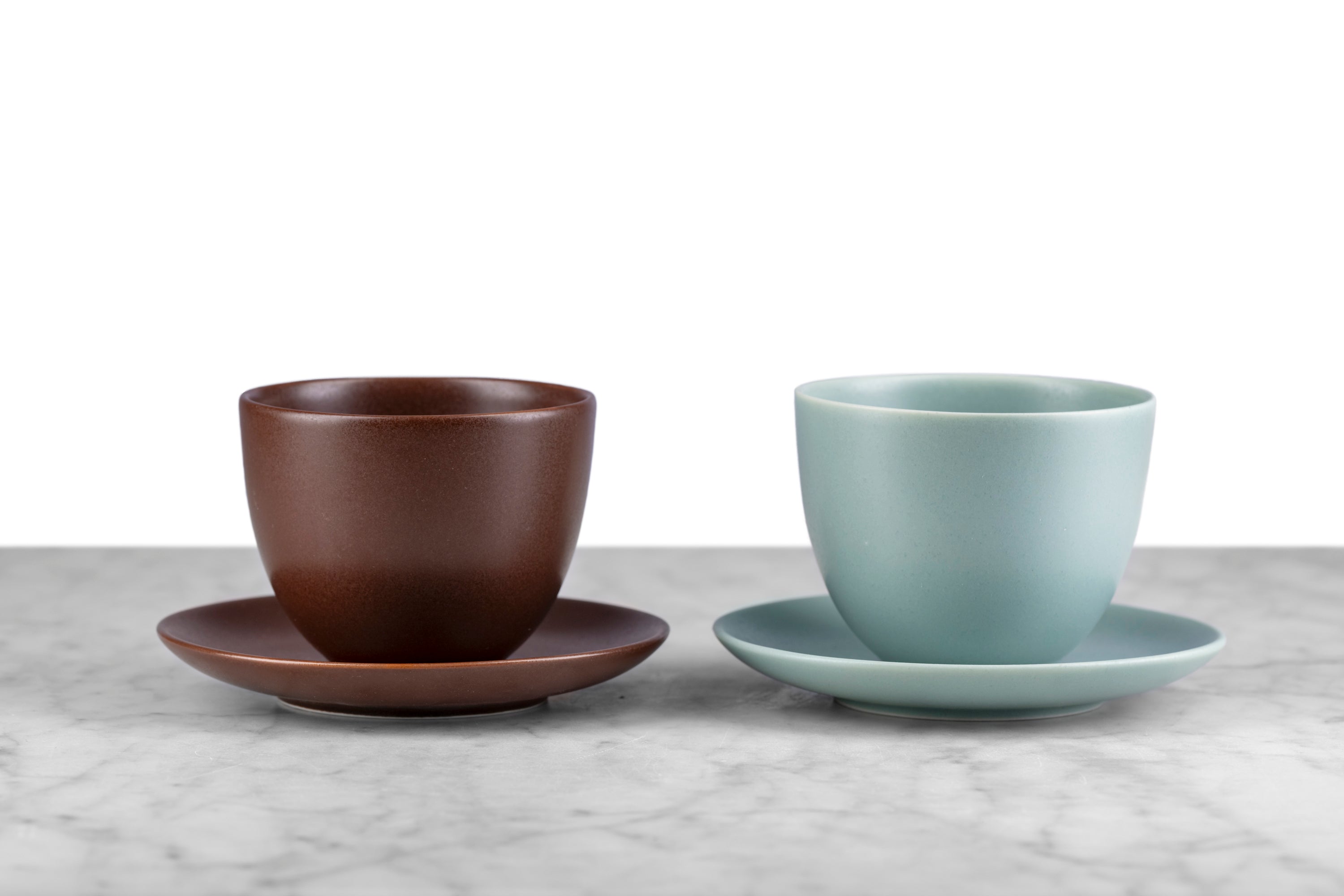 kinto pebble modern Japanese teaware brown handleless cup and saucer and moss green handleless cup and saucer on marble with white background