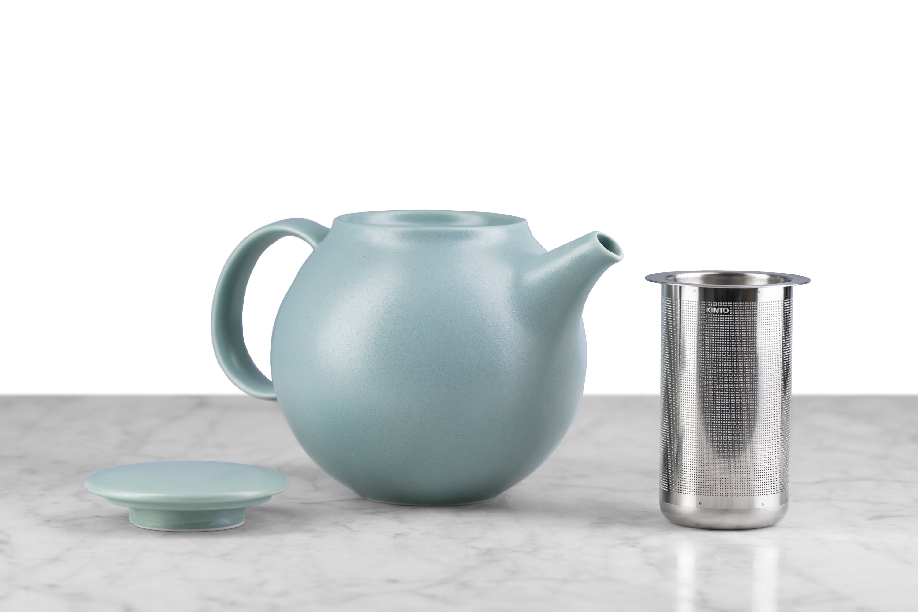 moss green kinto pebble modern teapot on marble with white background. Lid and infuser next to teapot.