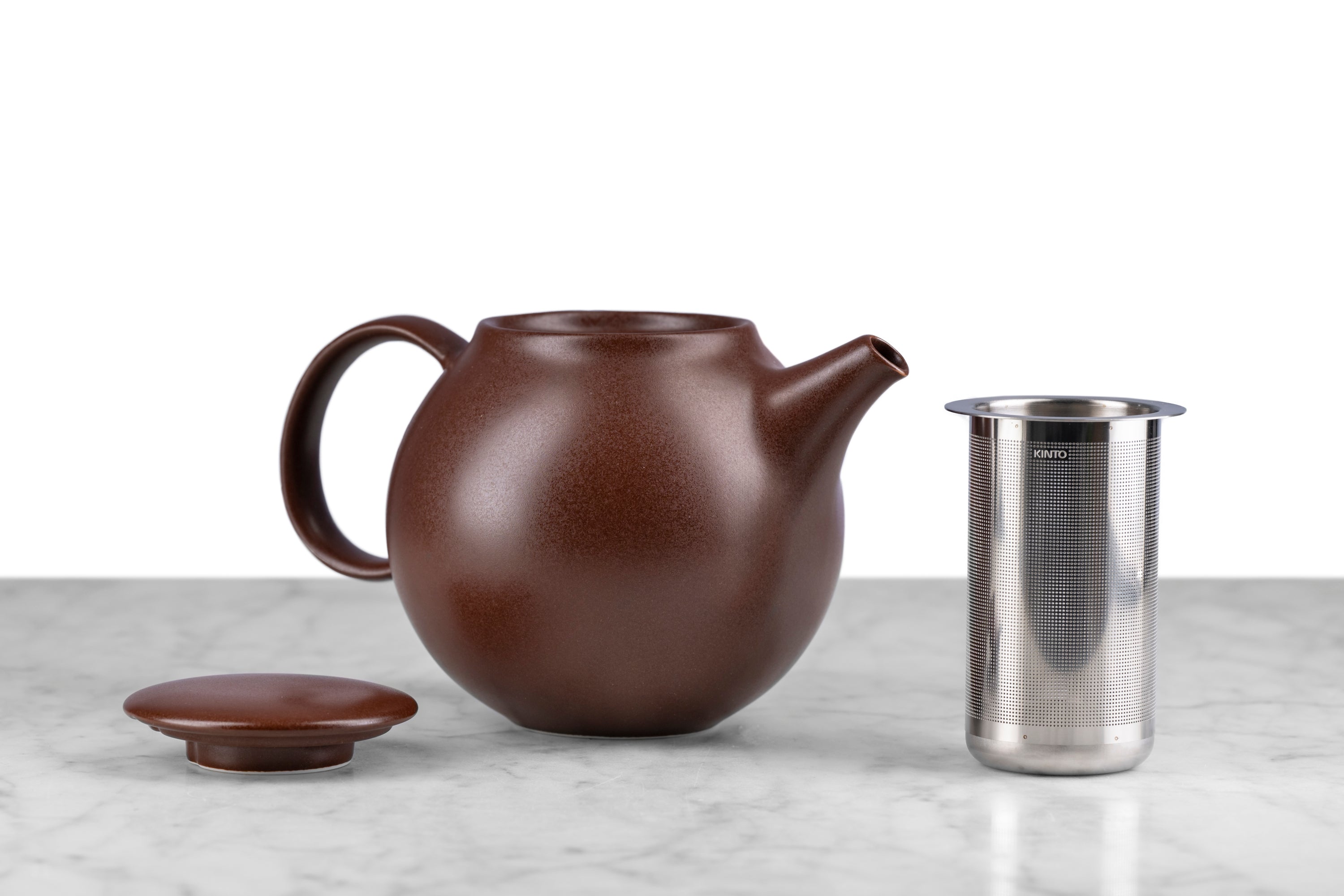 brown kinto pebble modern teapot on marble with white background. Lid and infuser next to teapot.
