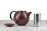 brown kinto pebble modern teapot on marble with white background. Lid and infuser next to teapot.