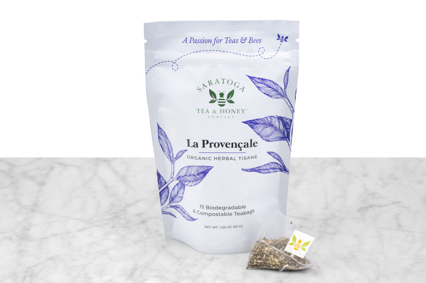 La Provençale tea sachets packaging and example sachet. A small pyramid tea sachet with visible brown and green leaves sits next to a pouch reading "La Provençale Organic Herbal Tisane. 15 Biodegradable & Compostable Tea Bags."