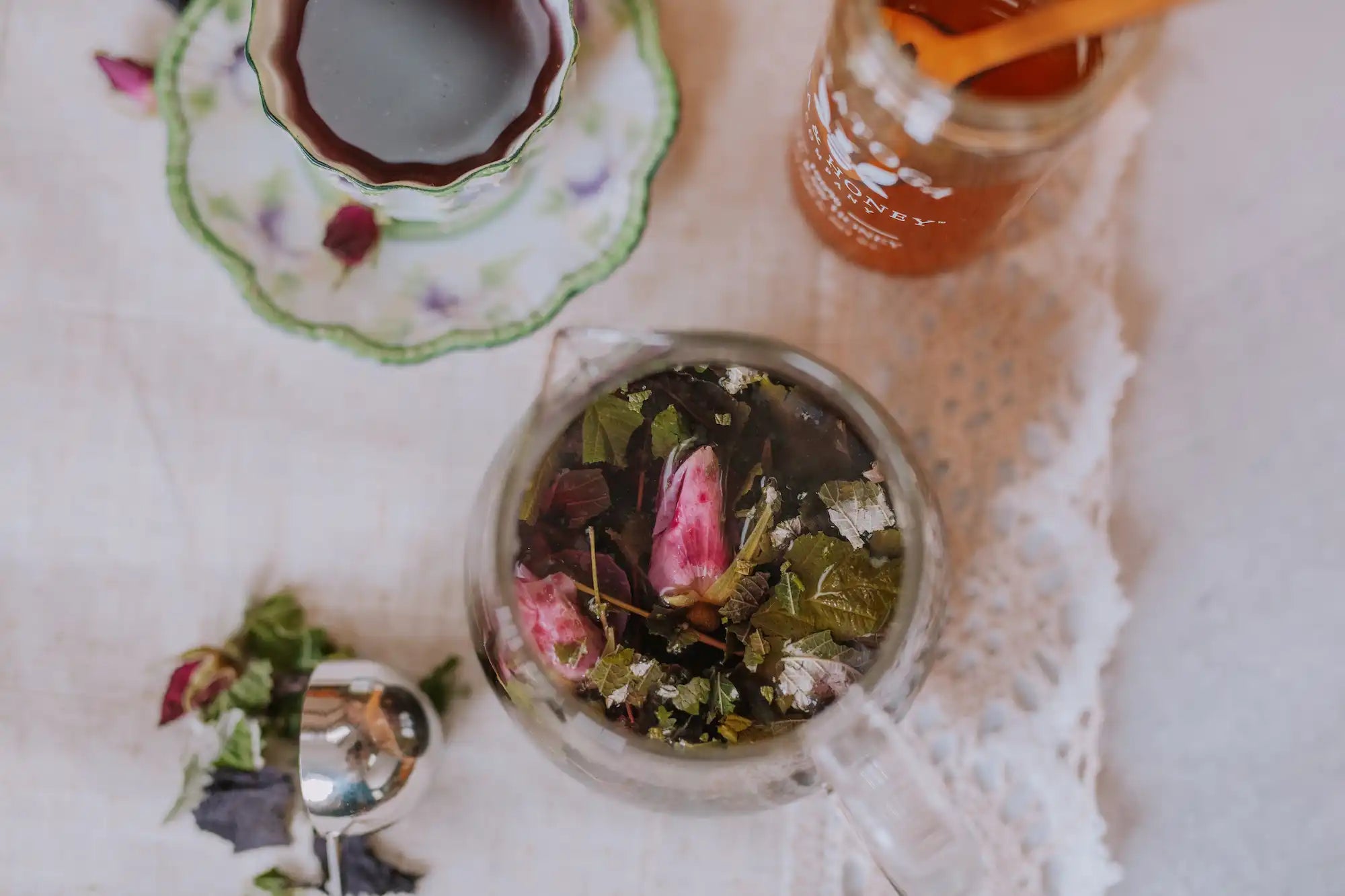 la vie en rose herbal tisane in a glass teapot with poured cup of purple herbal tea in a vintage cup