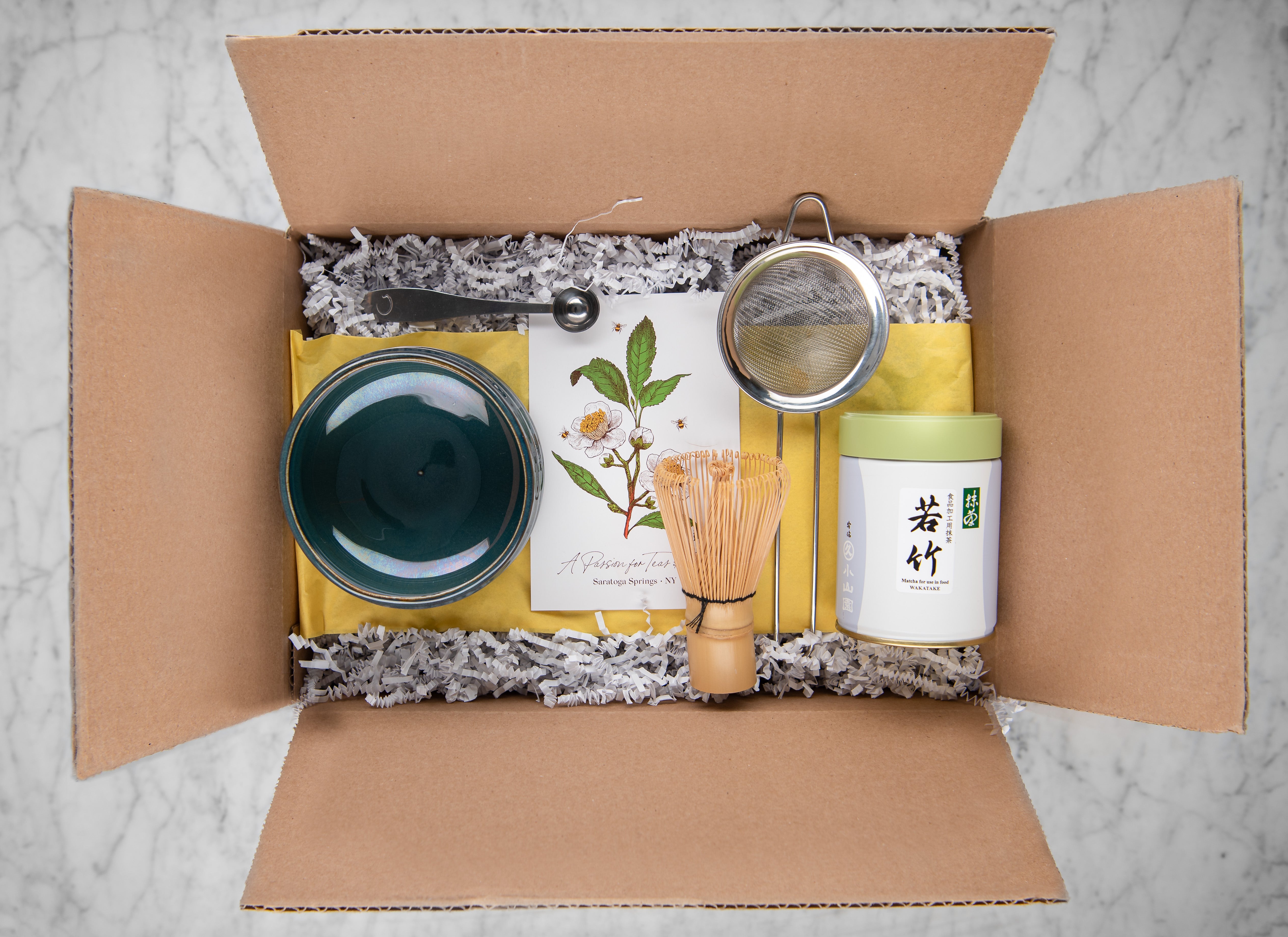 gift box with decorative fill featuring a jade matcha bowl, matcha whisk, tin of premium grade wakatake matcha, stainless steel sifter and perfect matcha spoon