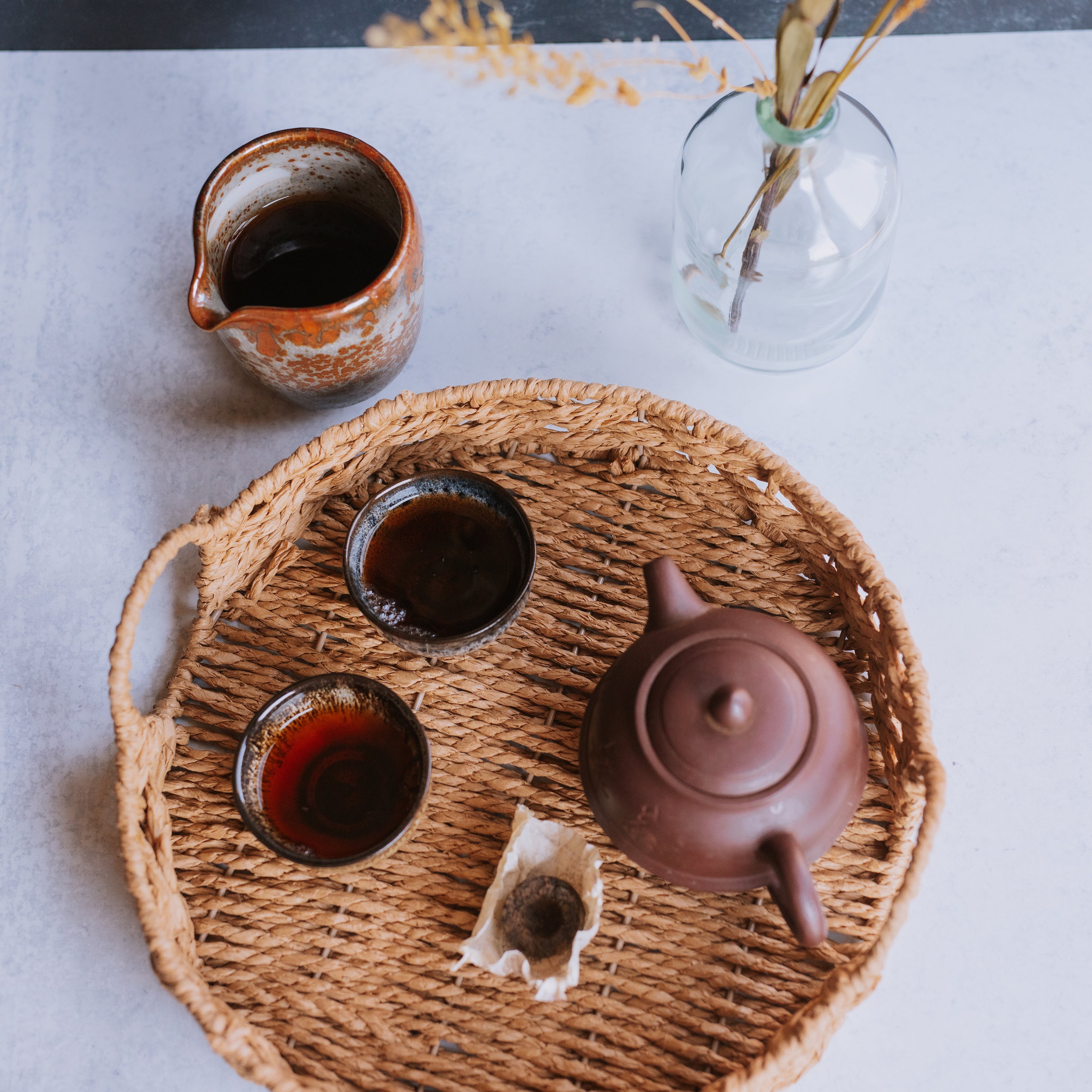 pitcher, two cups, and small yixing pot of pu erh aged tea on a woven tray