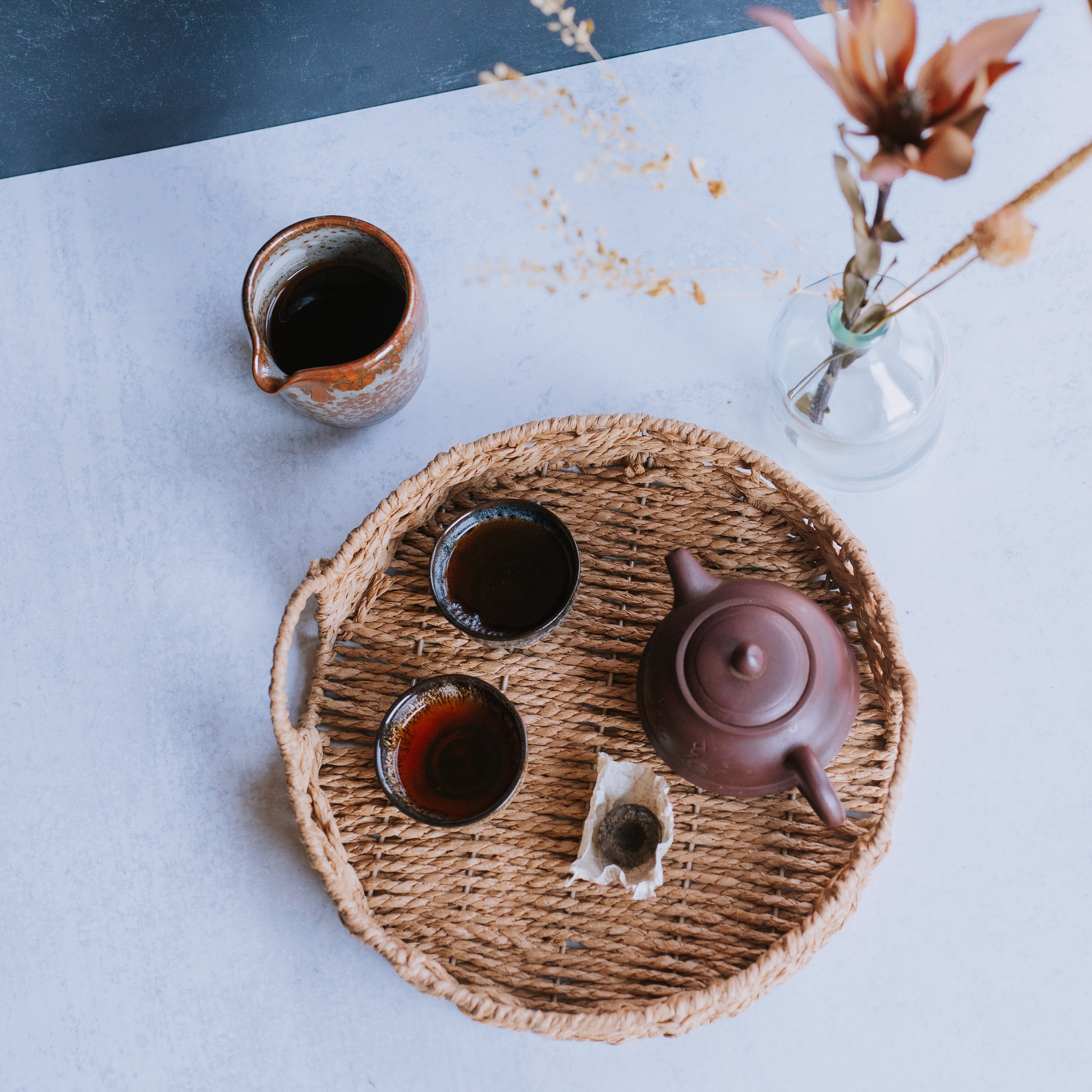 earthenware pitcher of brewed pu erh tea sitting next to a woven basket tray with two cups of pu erh, a yixing clay pot, and a mini toucha of 2012 Menghai tea