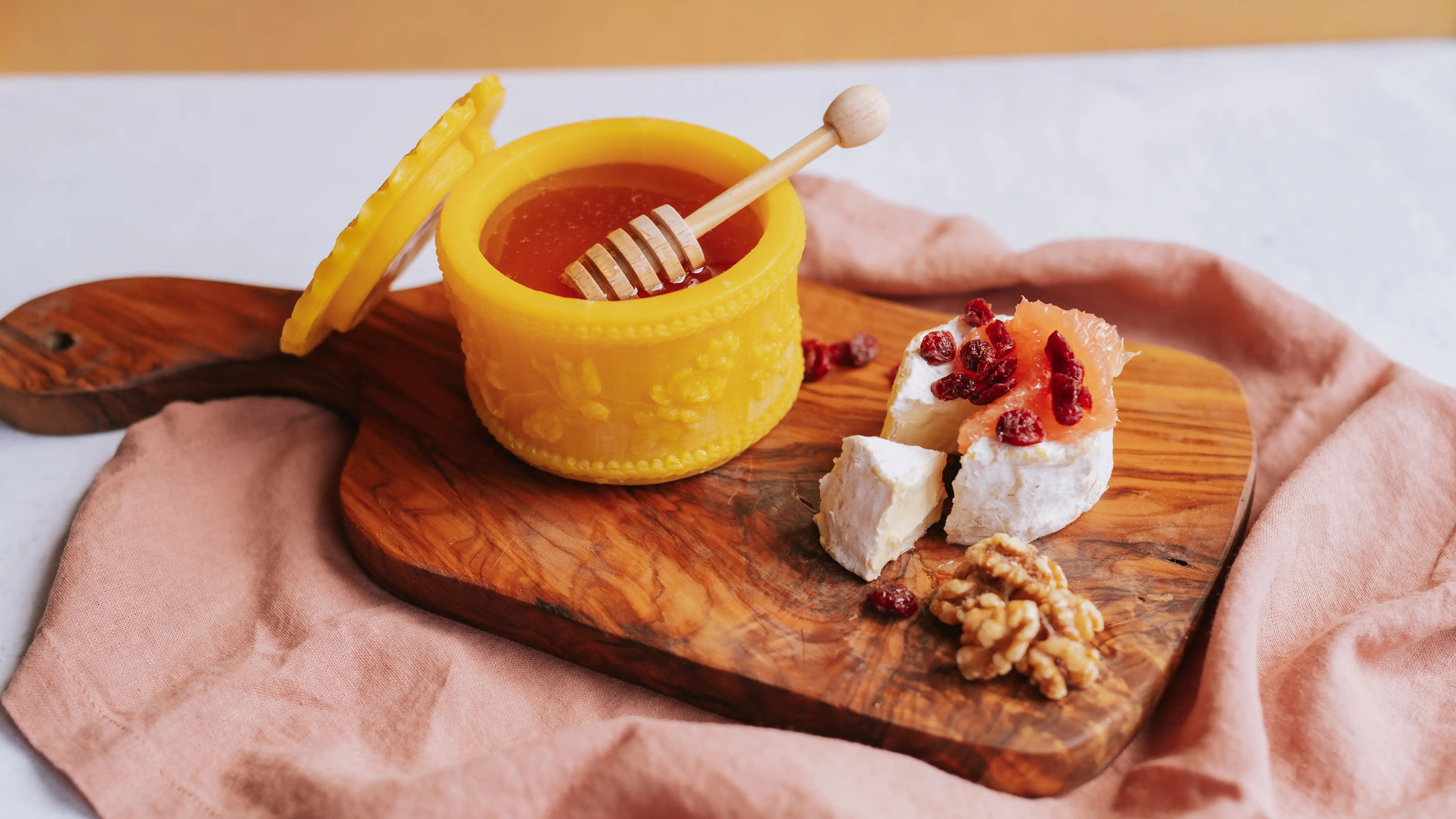beeswax honey pot full of raw honey on a charcuterie board with brie and citrus and nuts