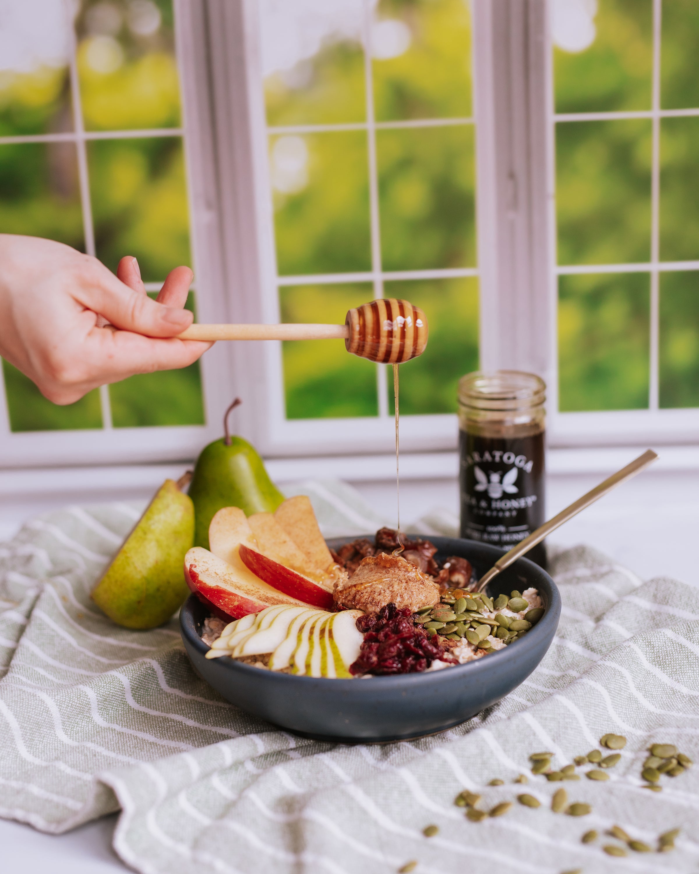 hand drizzling pumpkin spice honey over a breakfast power bowl with apples, pears, nutbutter, and dried fruit