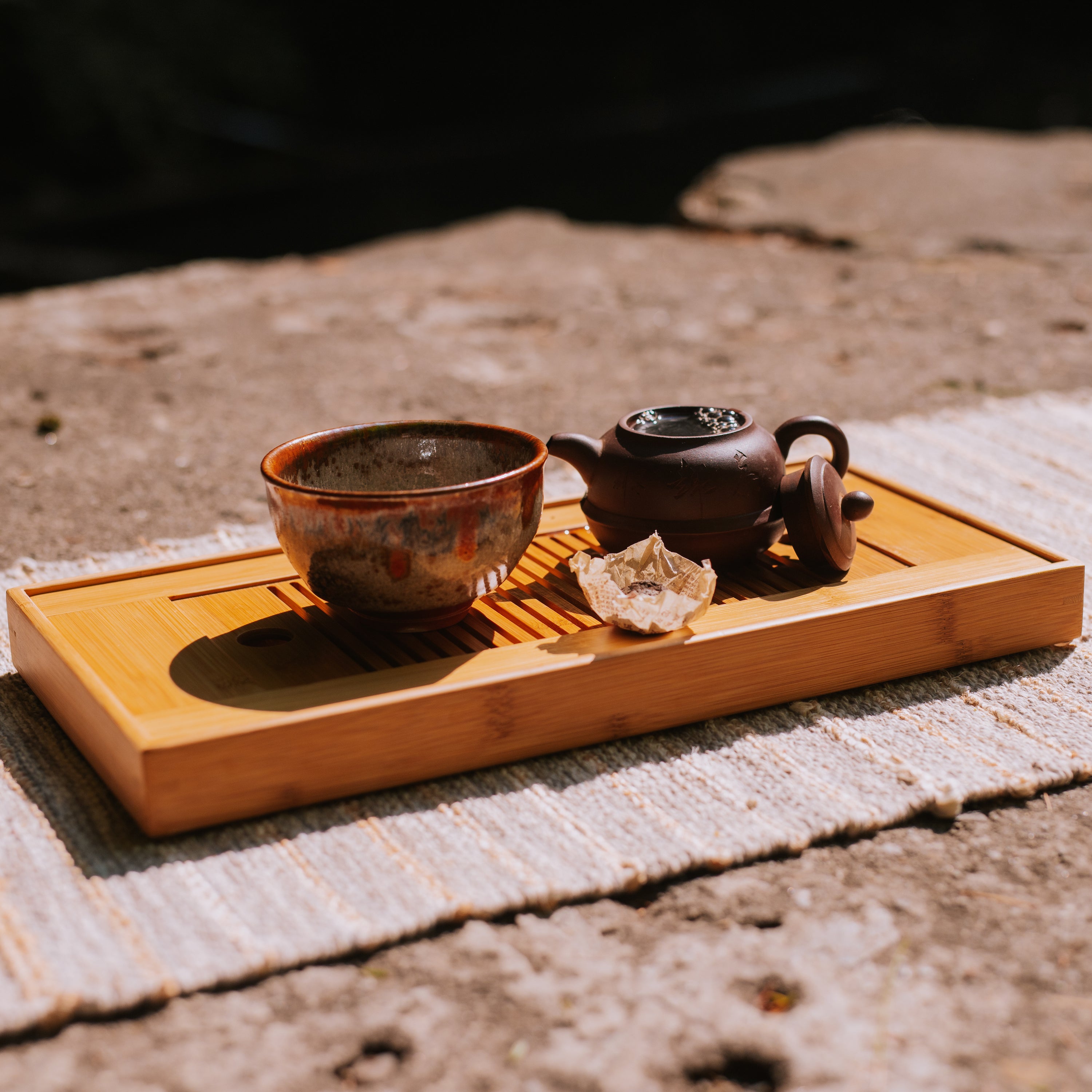 tea boat with tea bowl, yixing pot, and brewing aged tea sitting on a rock