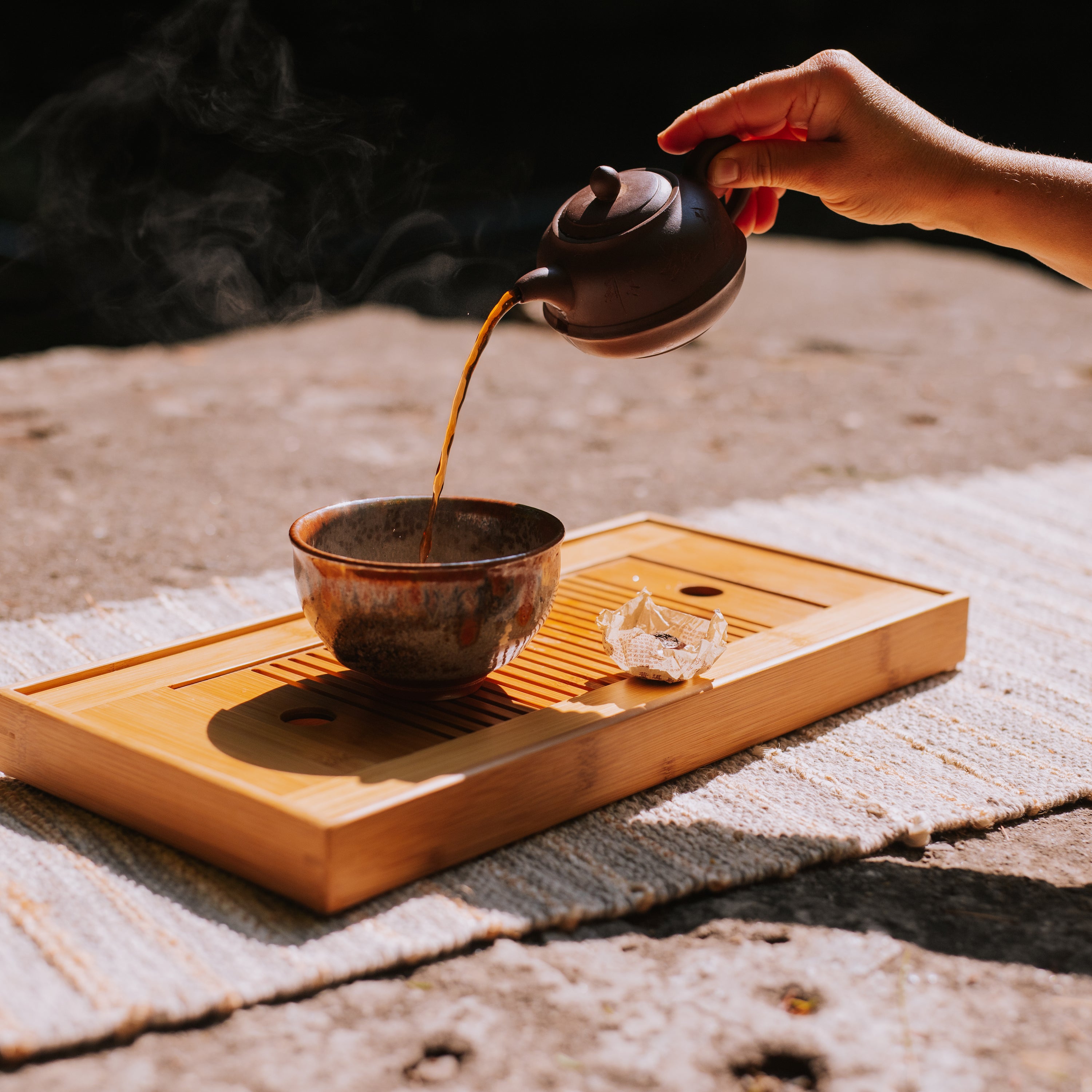hand pouring brewed pu erh tea from a small yixing teapot into a tea bowl