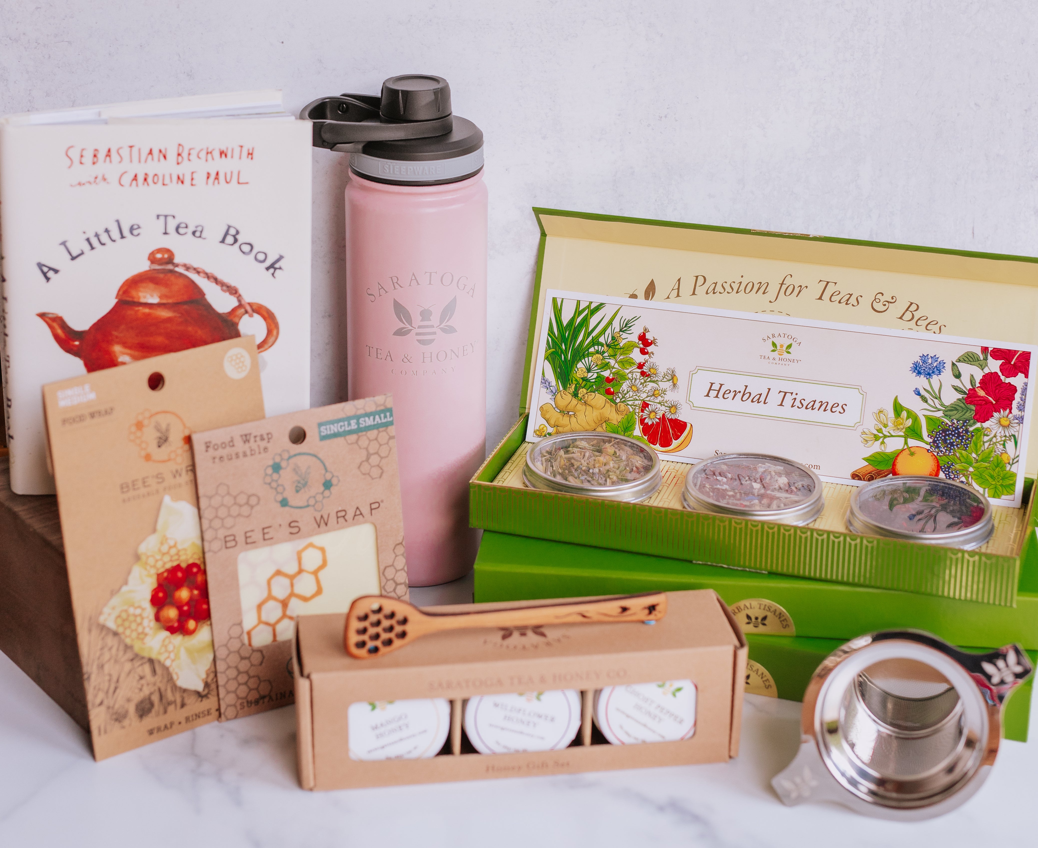 collection of tea and honey gifts from saratoga tea and honey co including a little tea book, tea tumbler, bees wrap, tea sample sets, honey sample sets, and accessories