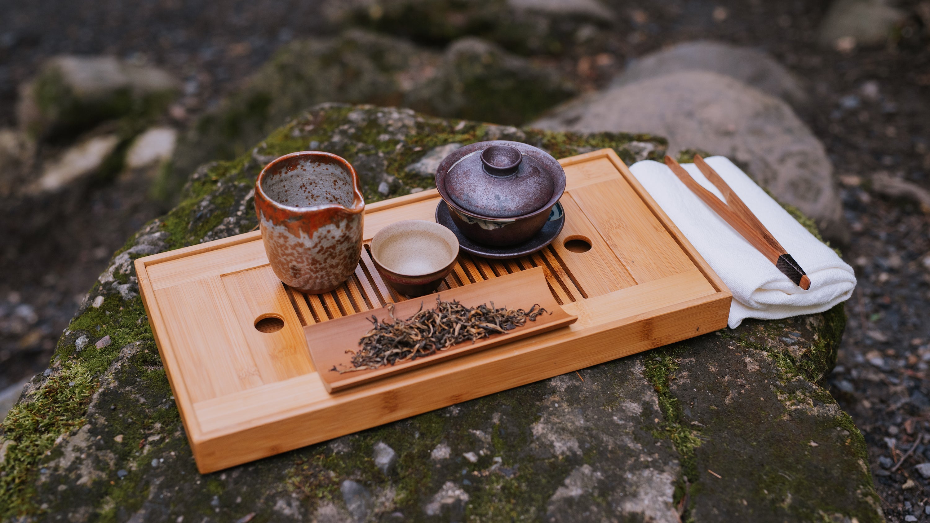 tea boat sitting on rock holding gaiwan, pitcher, small cup, and bamboo tea accessories
