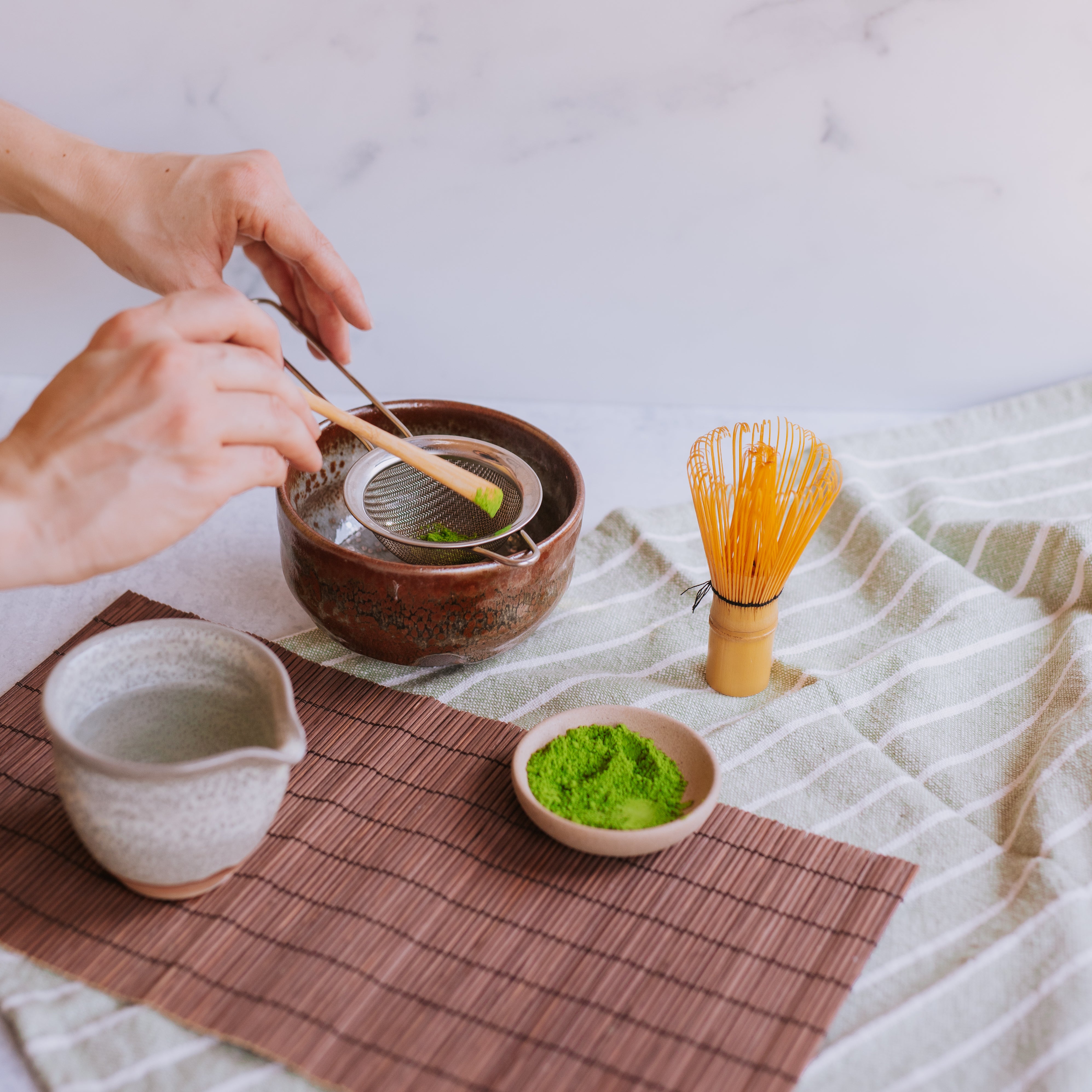 two hands measuring matcha into a matcha bowl with a bamboo scoop in preparation to make matcha