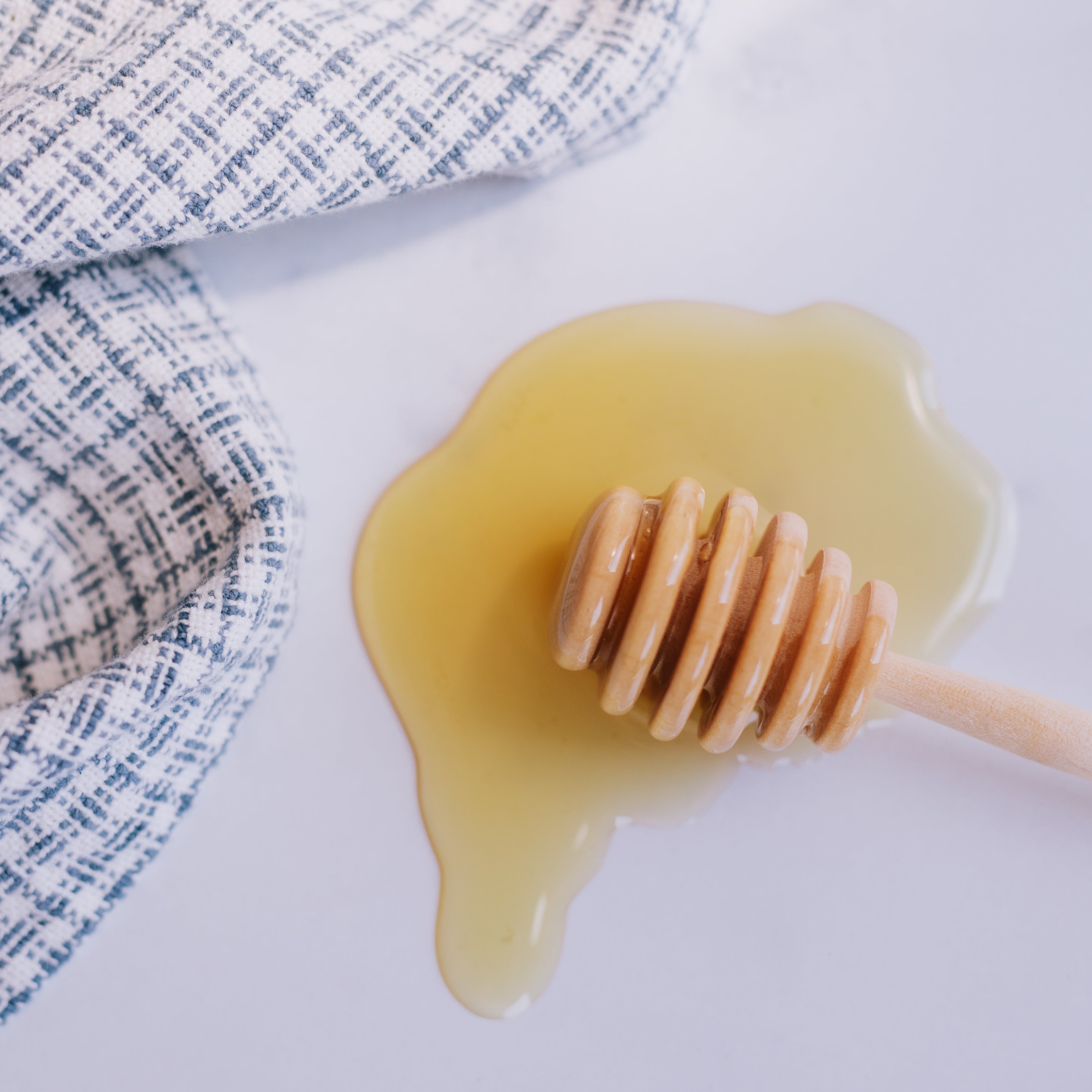 spilled golden honey with honey dipper and blue and white checked towel