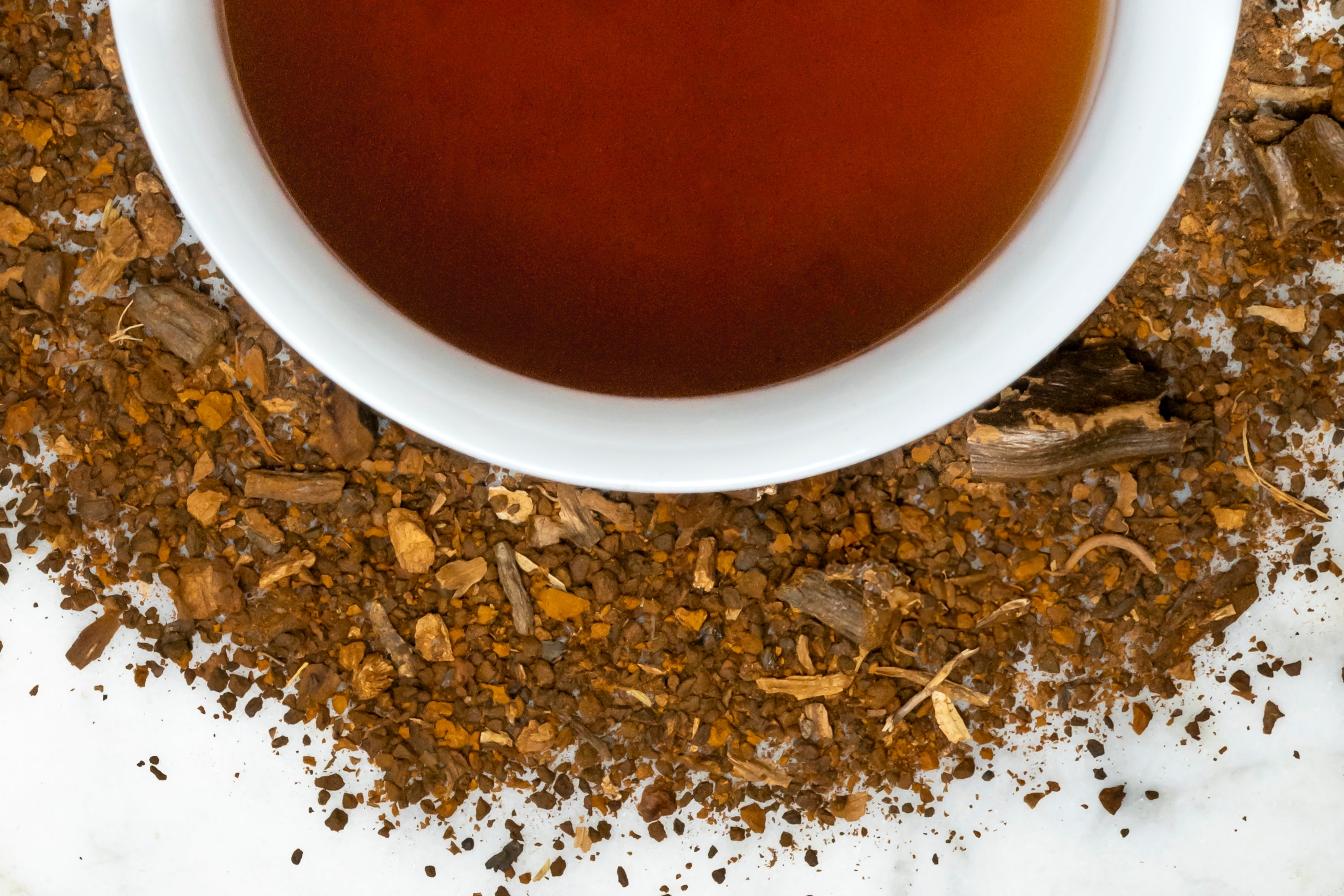 No Joe leaves and brewed tea. Powdered chaga mushroom, chicory root, and carob surround a cup of brewed, dark brown caffeine-free coffee alternative.