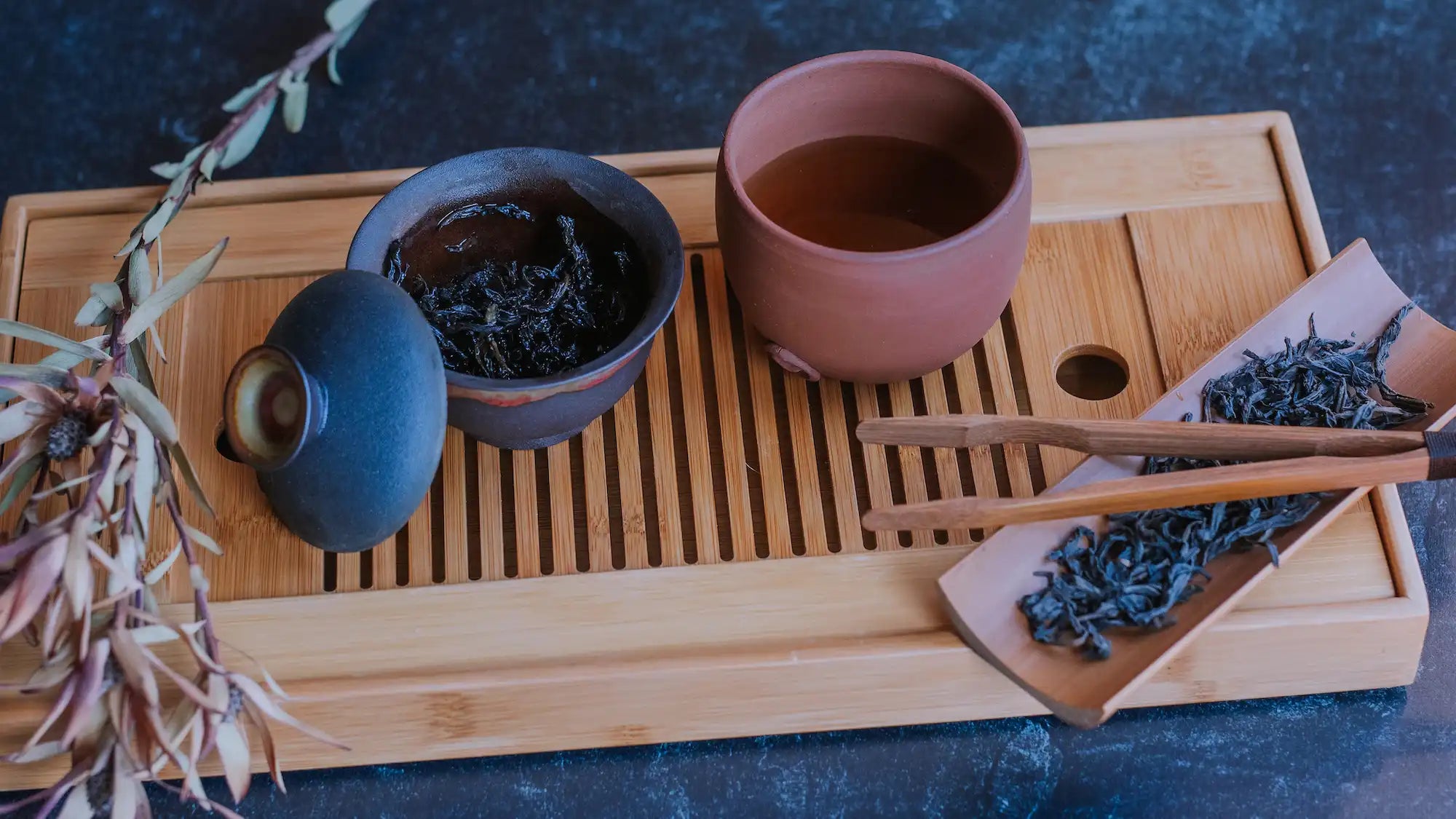 dark clay gaiwan of darkly oxidized oolong next to a tea bowl of oolong and loose leaf oolong tea on a tea boat