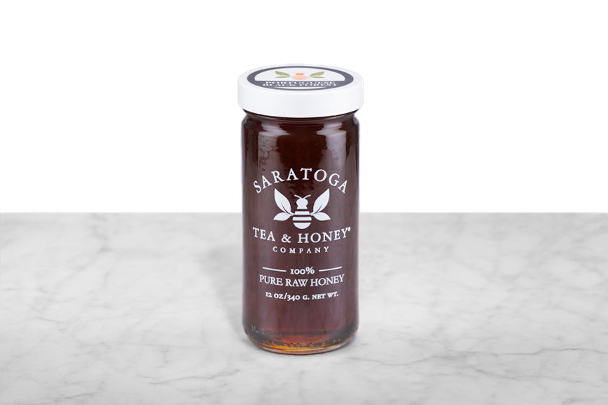 Dark amber-brown Portuguese Black Forest Honey displayed in a 12oz cylindrical glass jar with a white lid. The logo and the words: "100% Pure Raw Honey" are printed on the jar.