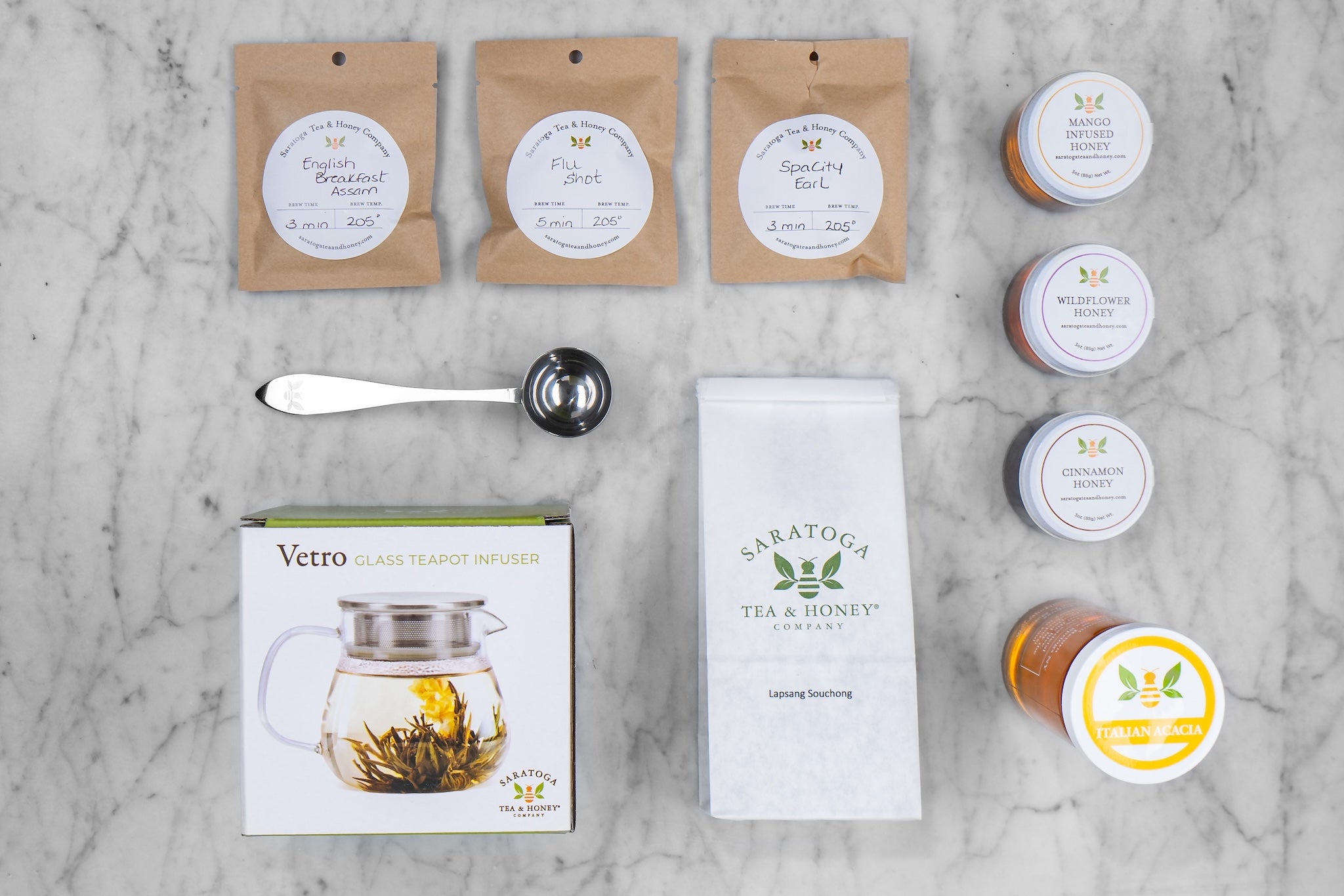 queen bee subscription box flat lay showing the three tea samples, three honey samples, tea scoop, glass teapot, tea of the month, and a 12oz european honey