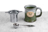 stainless steel tea infuser, tea scoop, and saratoga tea and honey co branded mug on a marble and white background