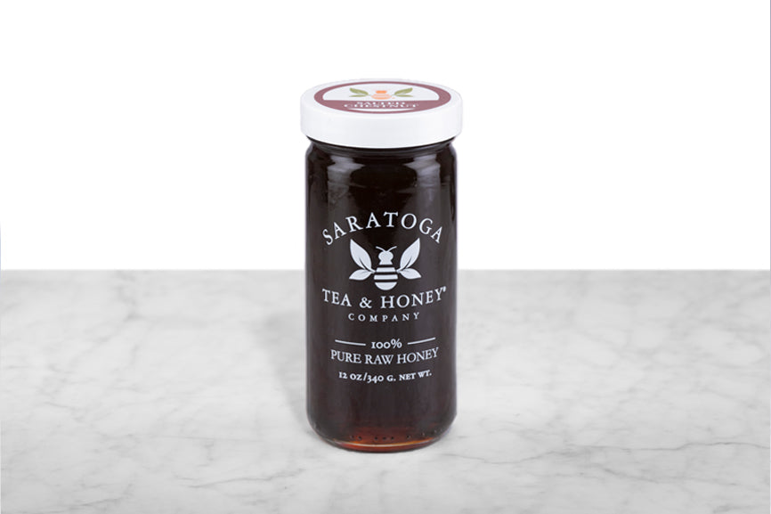 Very dark brown Salted Chestnut Honey displayed in a 12oz cylindrical glass jar with a white lid. The logo and the words: "100% Pure Raw Honey" are printed on the jar.