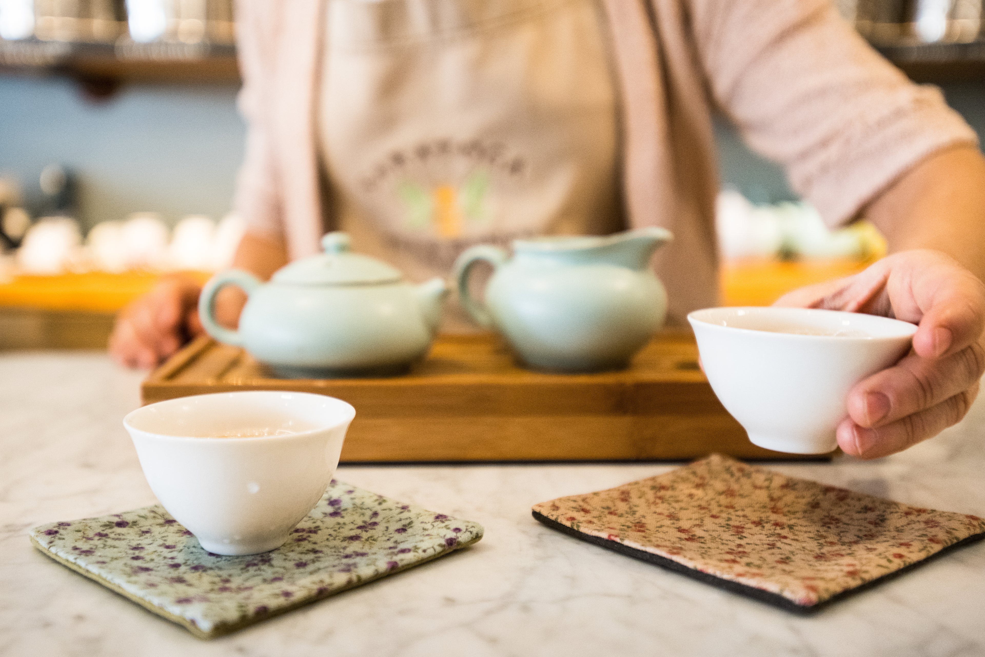woman presenting small white cup of Taiwanese oolong brewed in a traditional ruyao pancake teapot