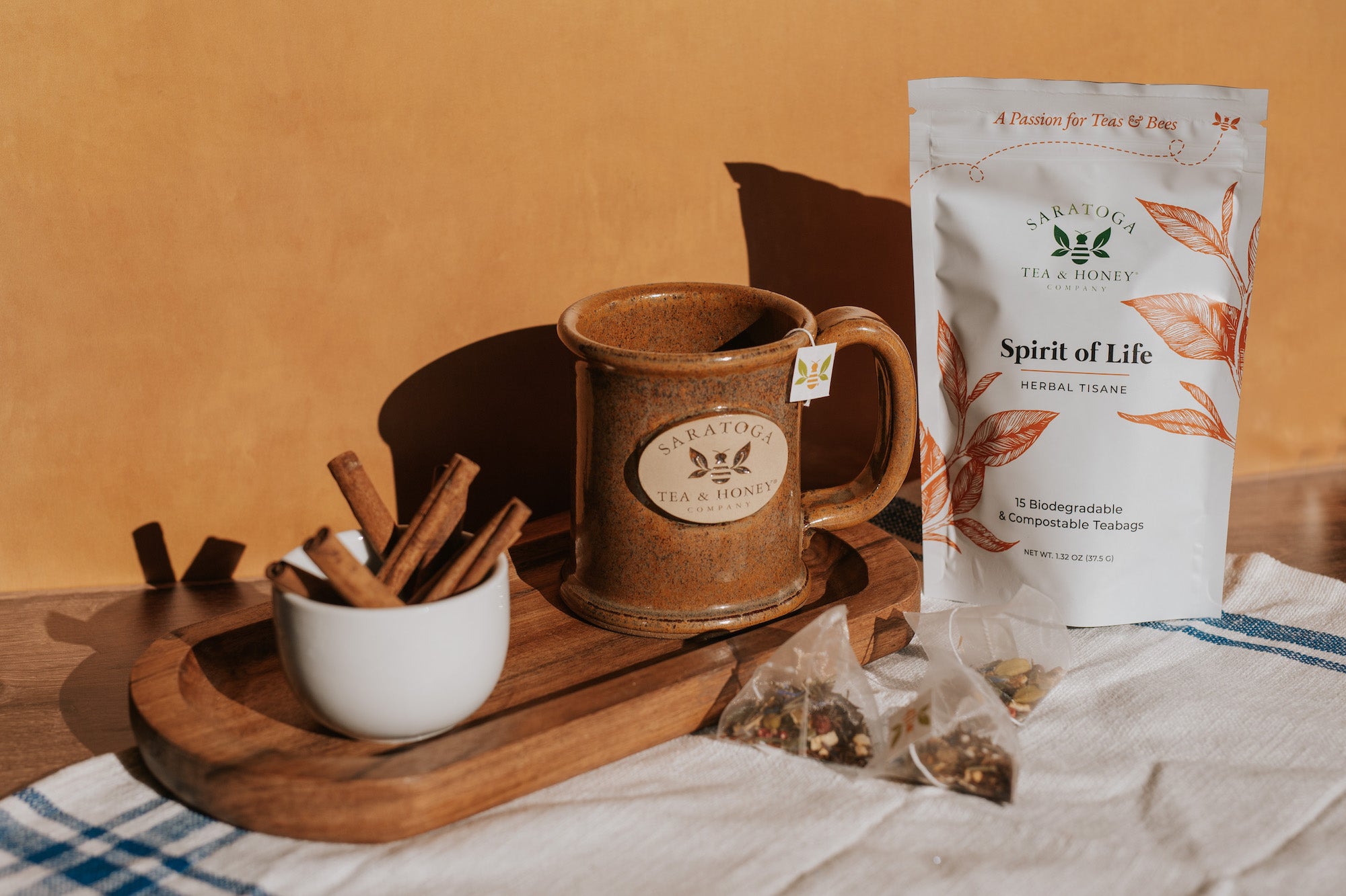 spirit of life citrus and spice herbal tisane tea sachets next to brown saratoga tea and honey co stoneware bee mug