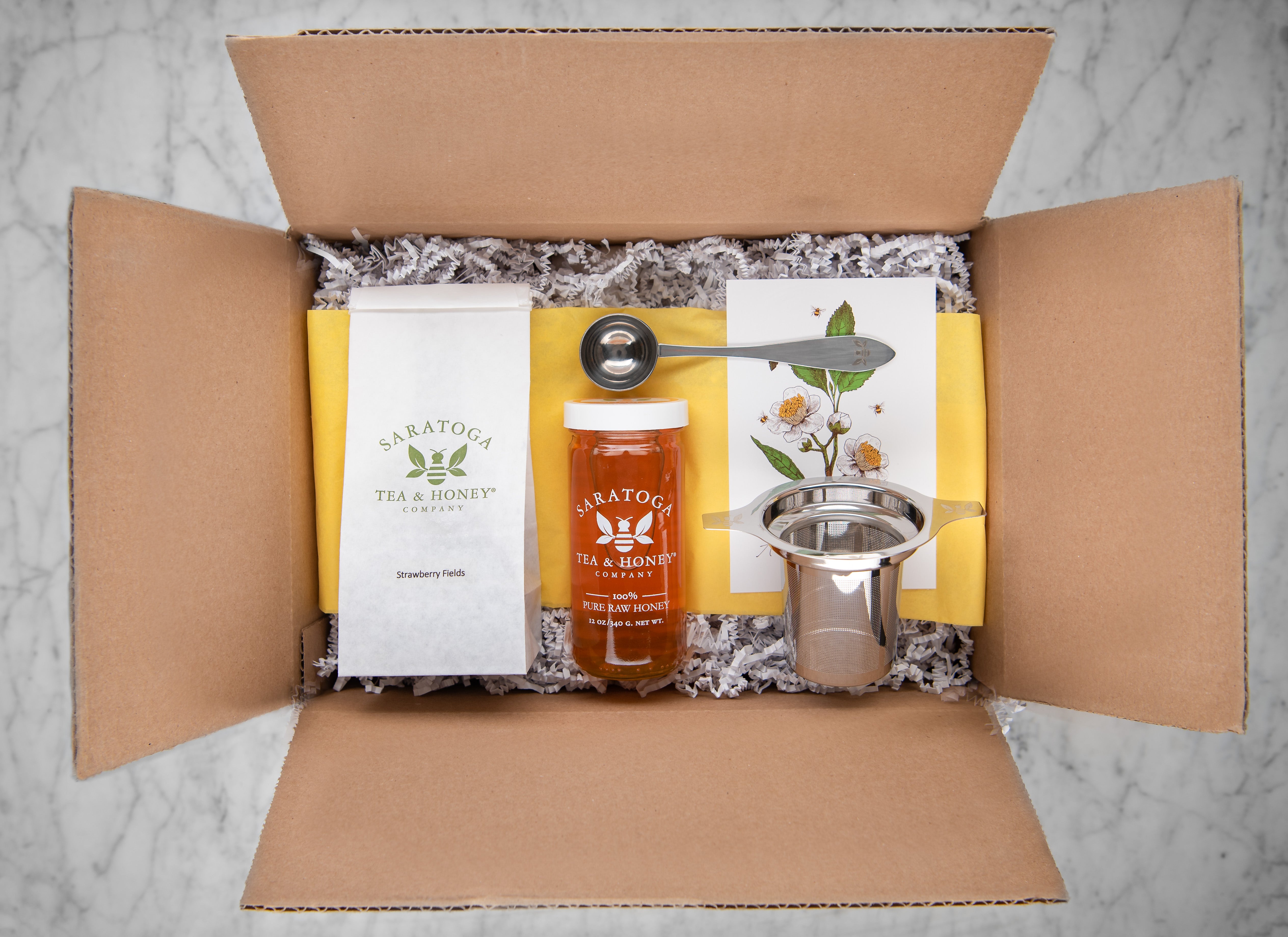 summer tea and honey box: cardboard box with decorative fill, strawberry fields tea, mango infused honey, tea infuser, and tea scoop