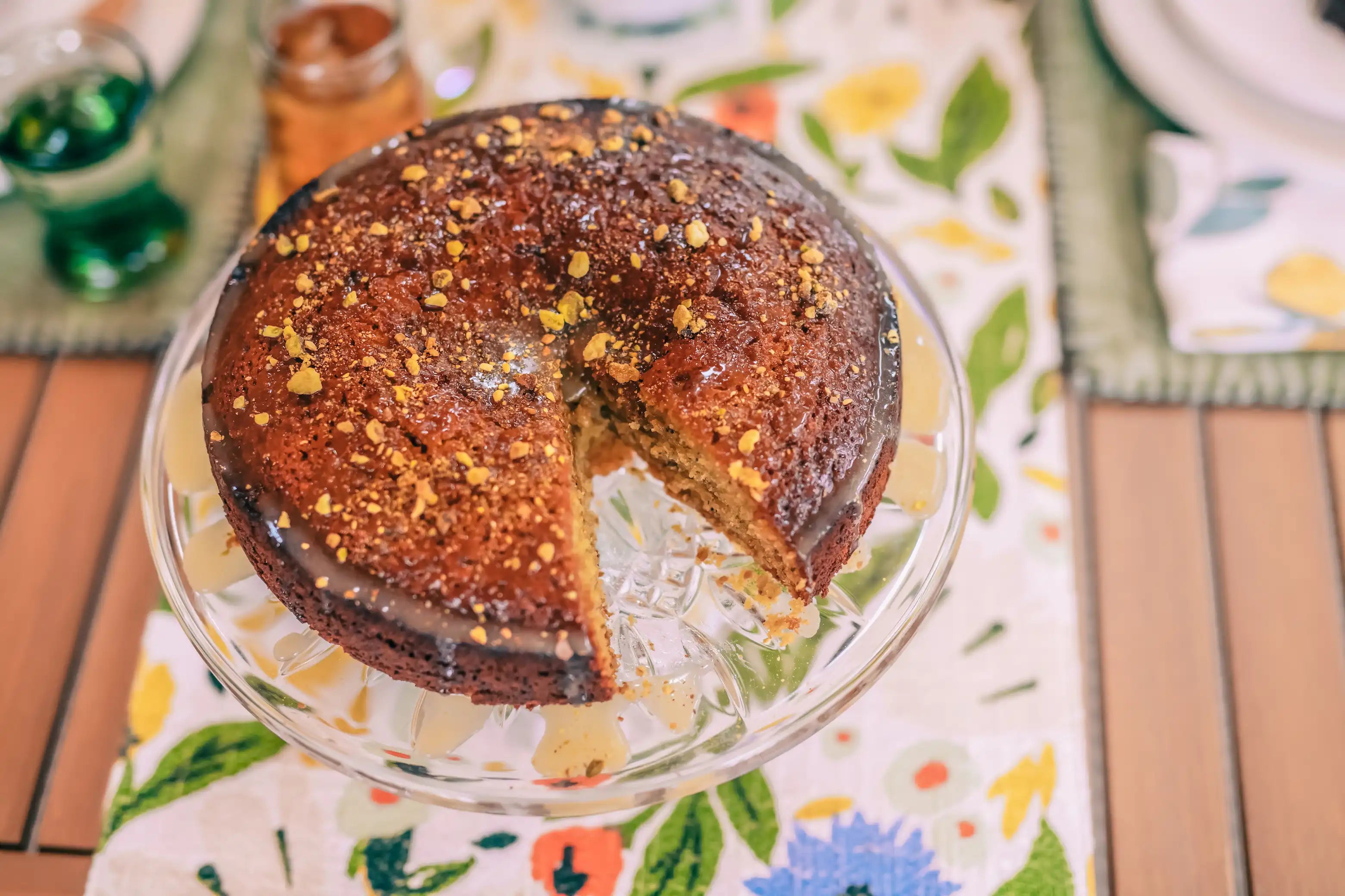 honey orange cardamom pistachio olive oil cake with a piece cut out at a summer party